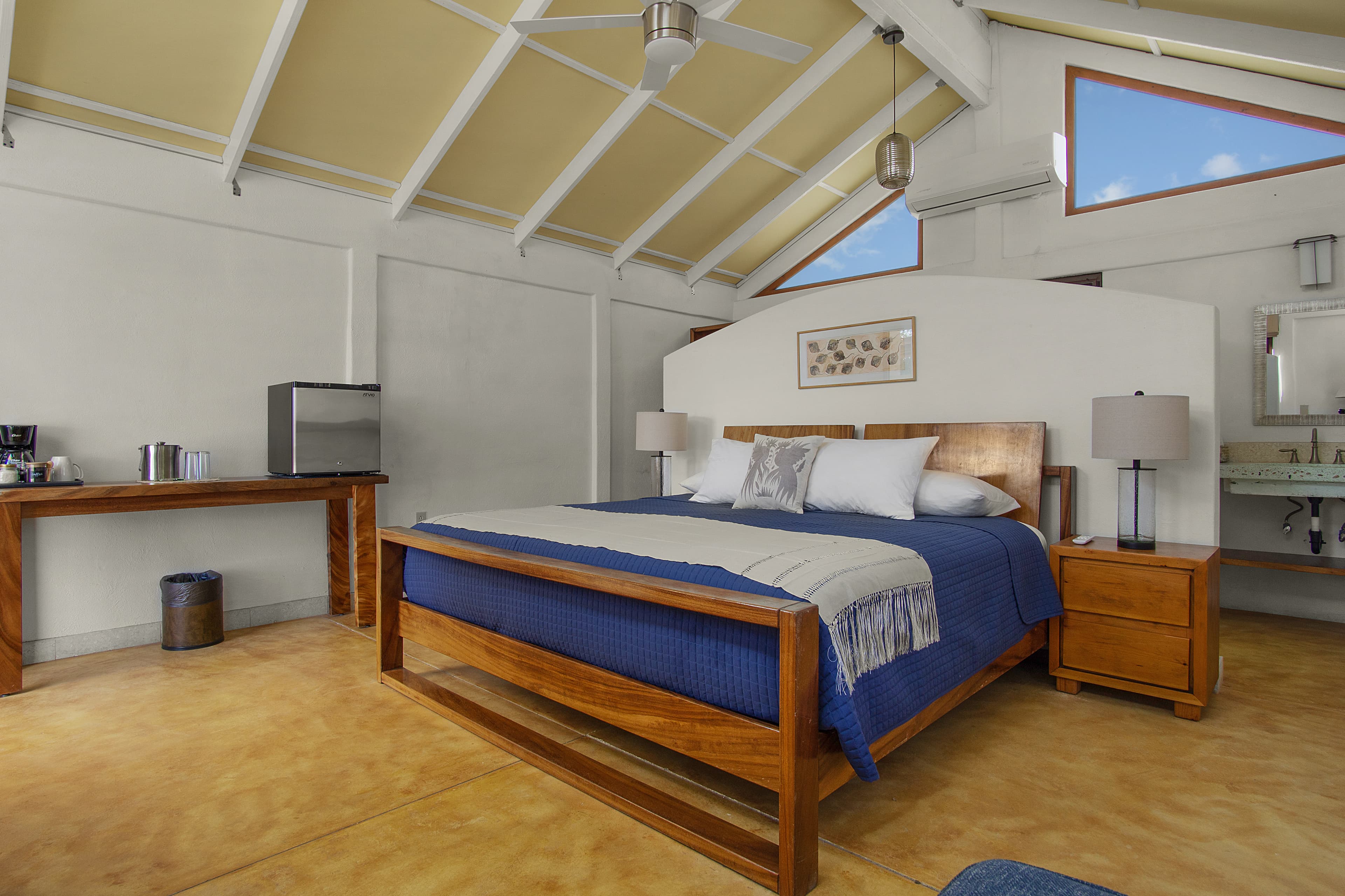 A spacious bedroom featuring a wooden bed, blue bedding, and a small kitchenette area.