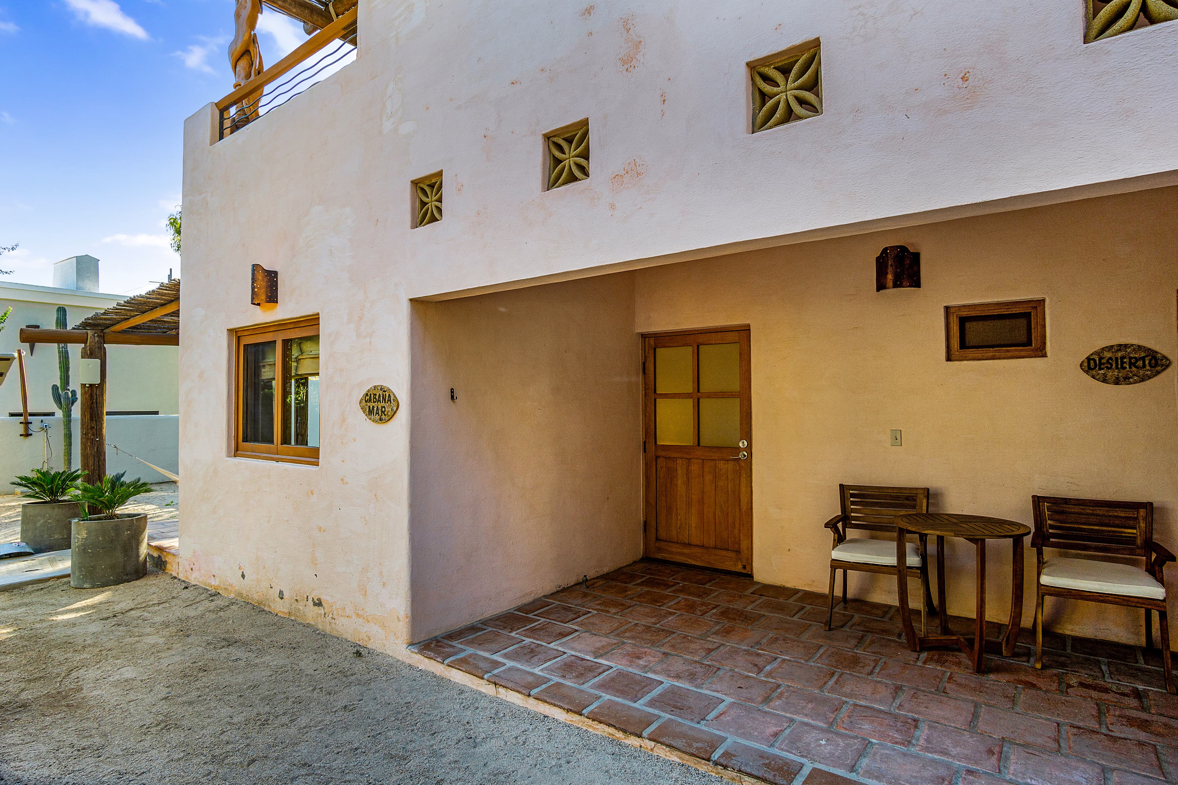 A serene entrance to a modest pink building with wooden accents and a small patio.
