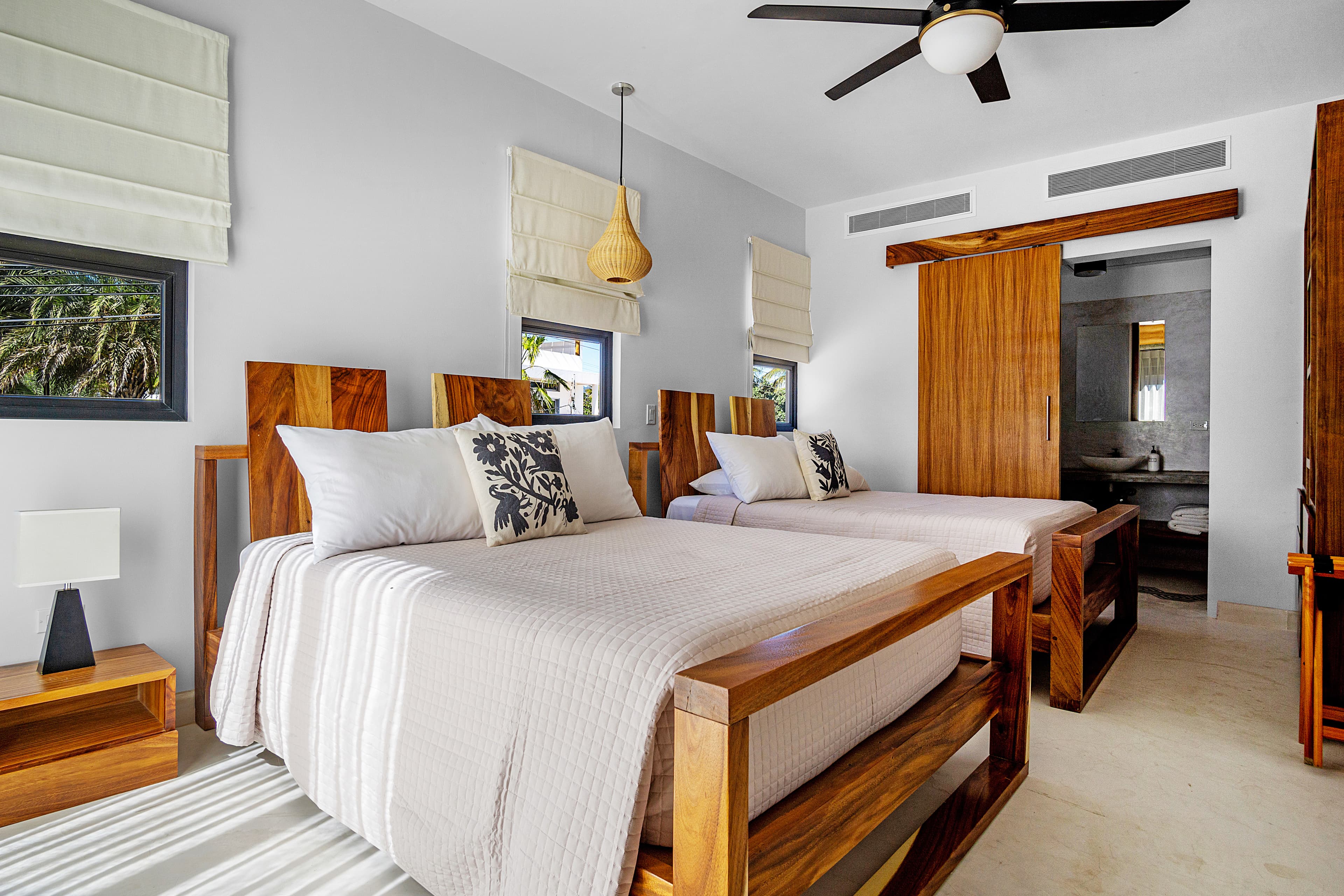 A modern bedroom featuring two wooden beds with white linens, a bedside table, and neutral decor.