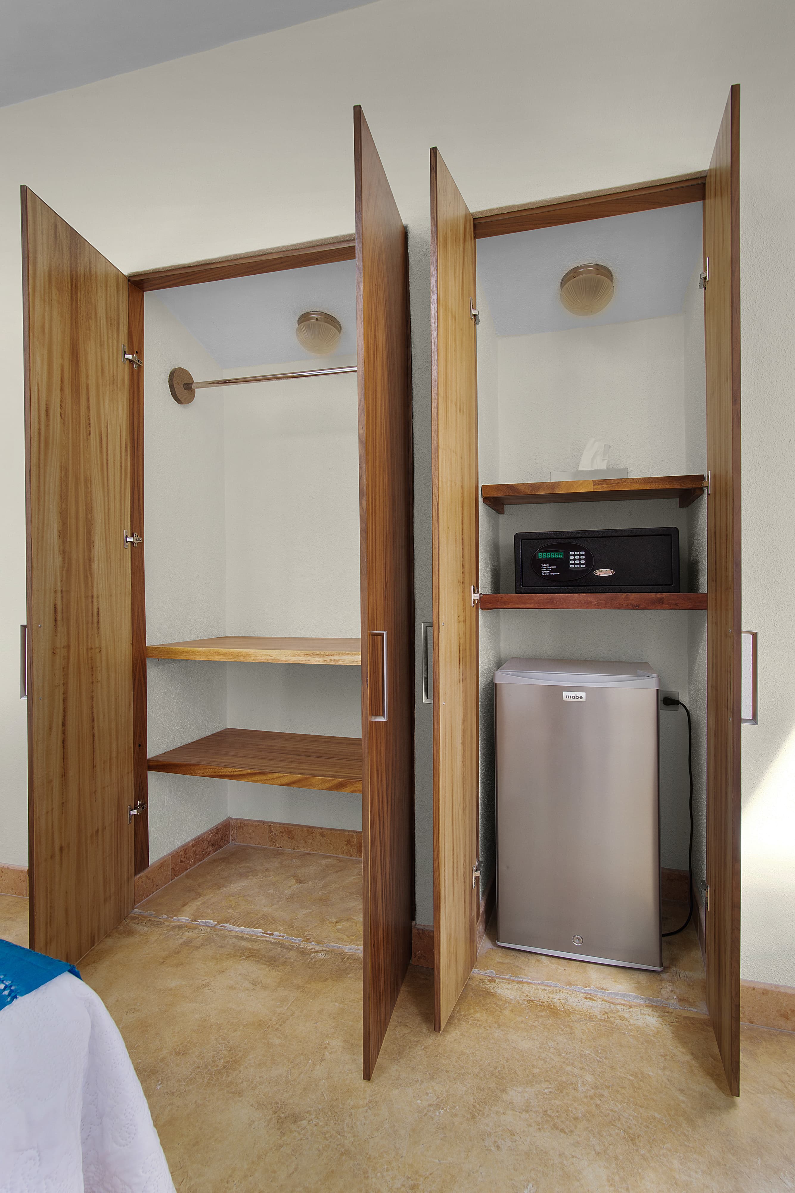 A wooden closet with two open doors revealing shelves and a small refrigerator.
