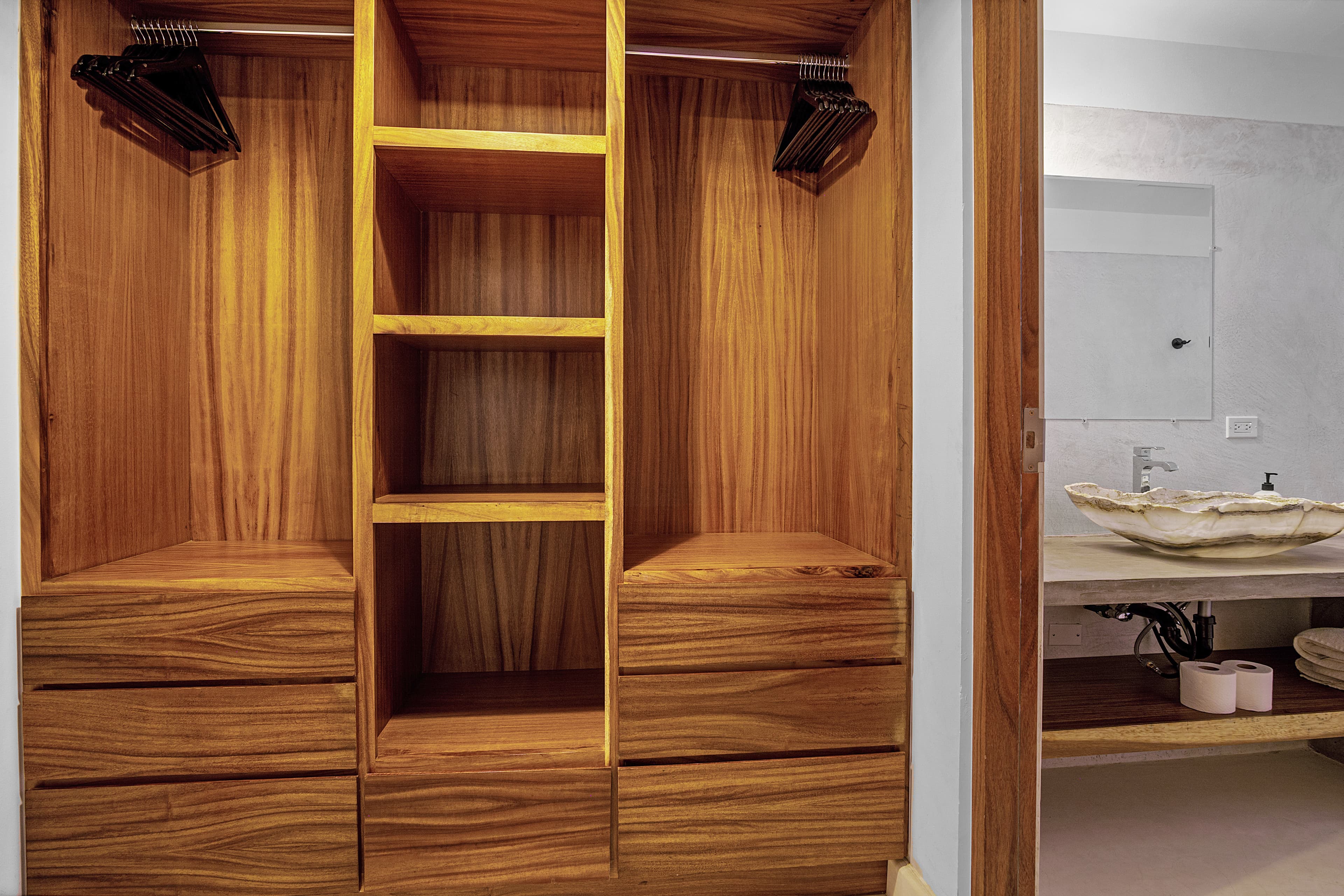 A wooden wardrobe with hanging space and four drawers, adjacent to a bathroom sink.