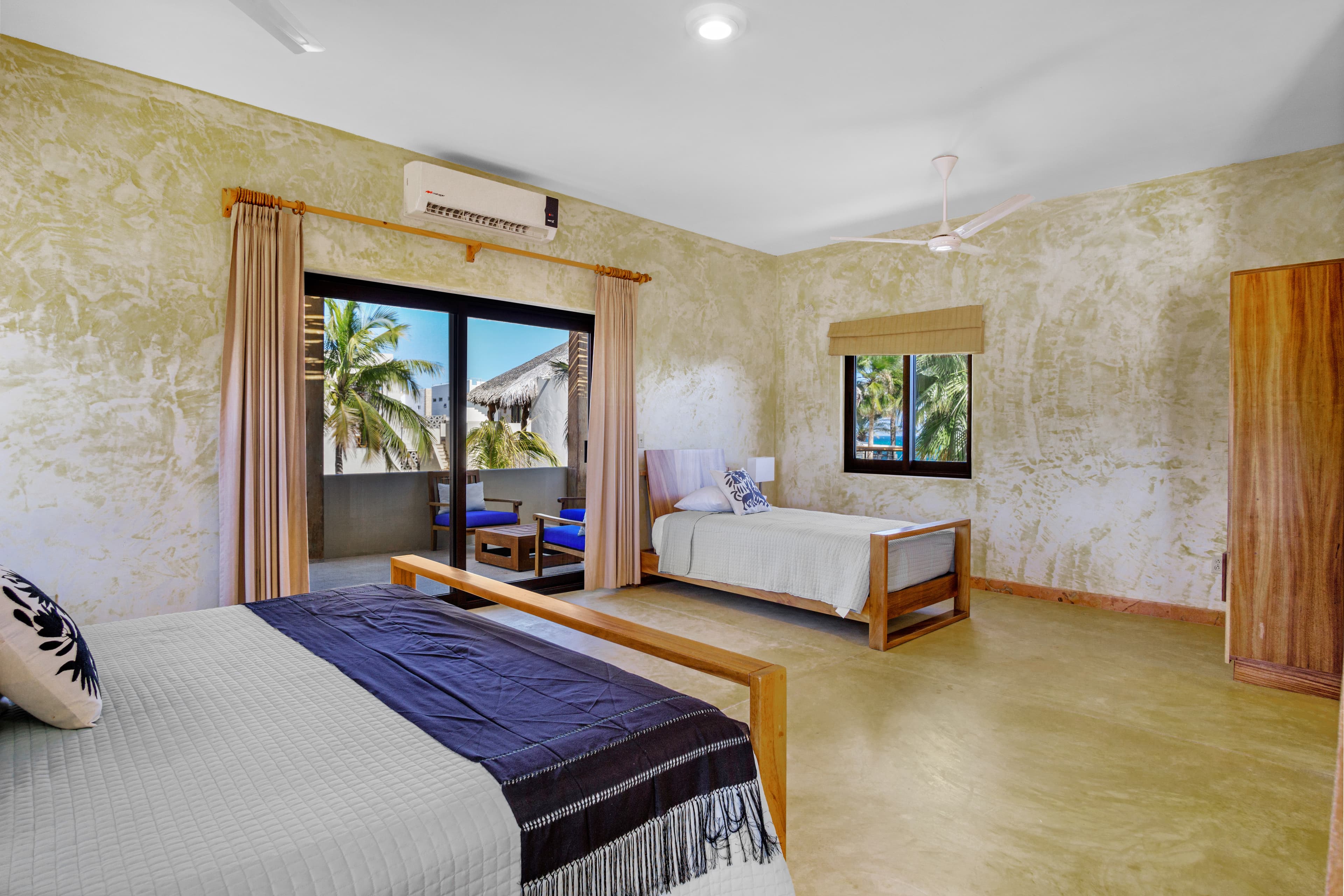 A spacious, minimally decorated bedroom with two beds and large windows showcasing palm trees outside.
