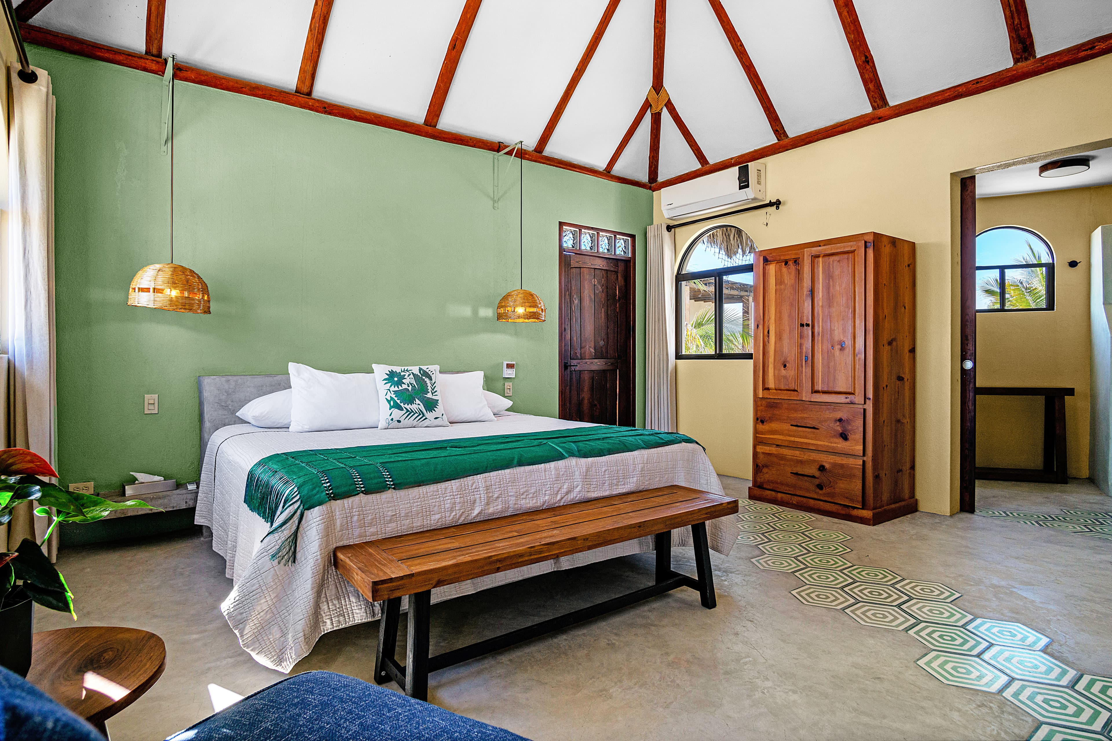 A cozy bedroom featuring a large bed, wooden bench, and decorative hanging lights against a green wall.
