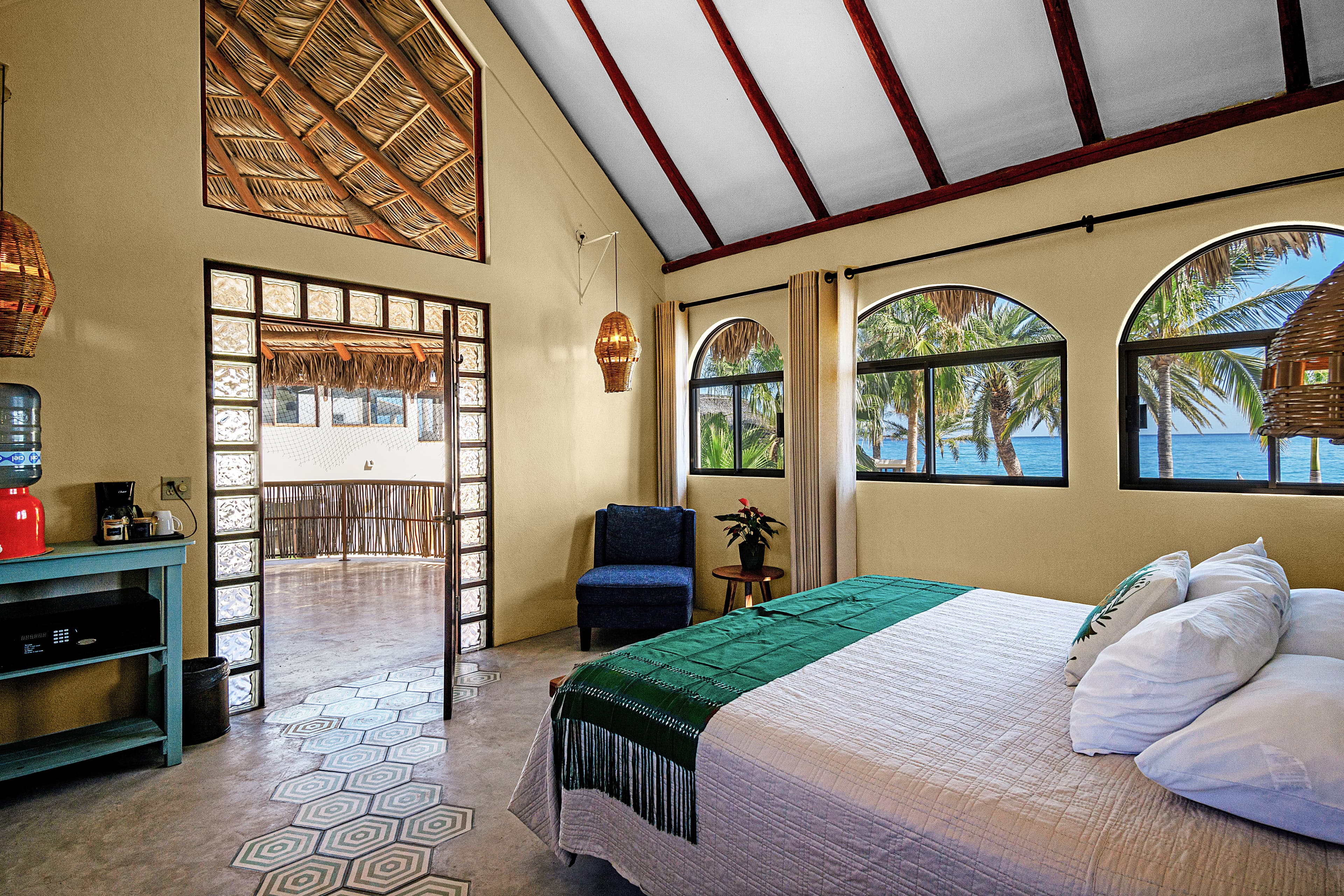Bright, airy bedroom with a view of palm trees and the ocean through large windows.