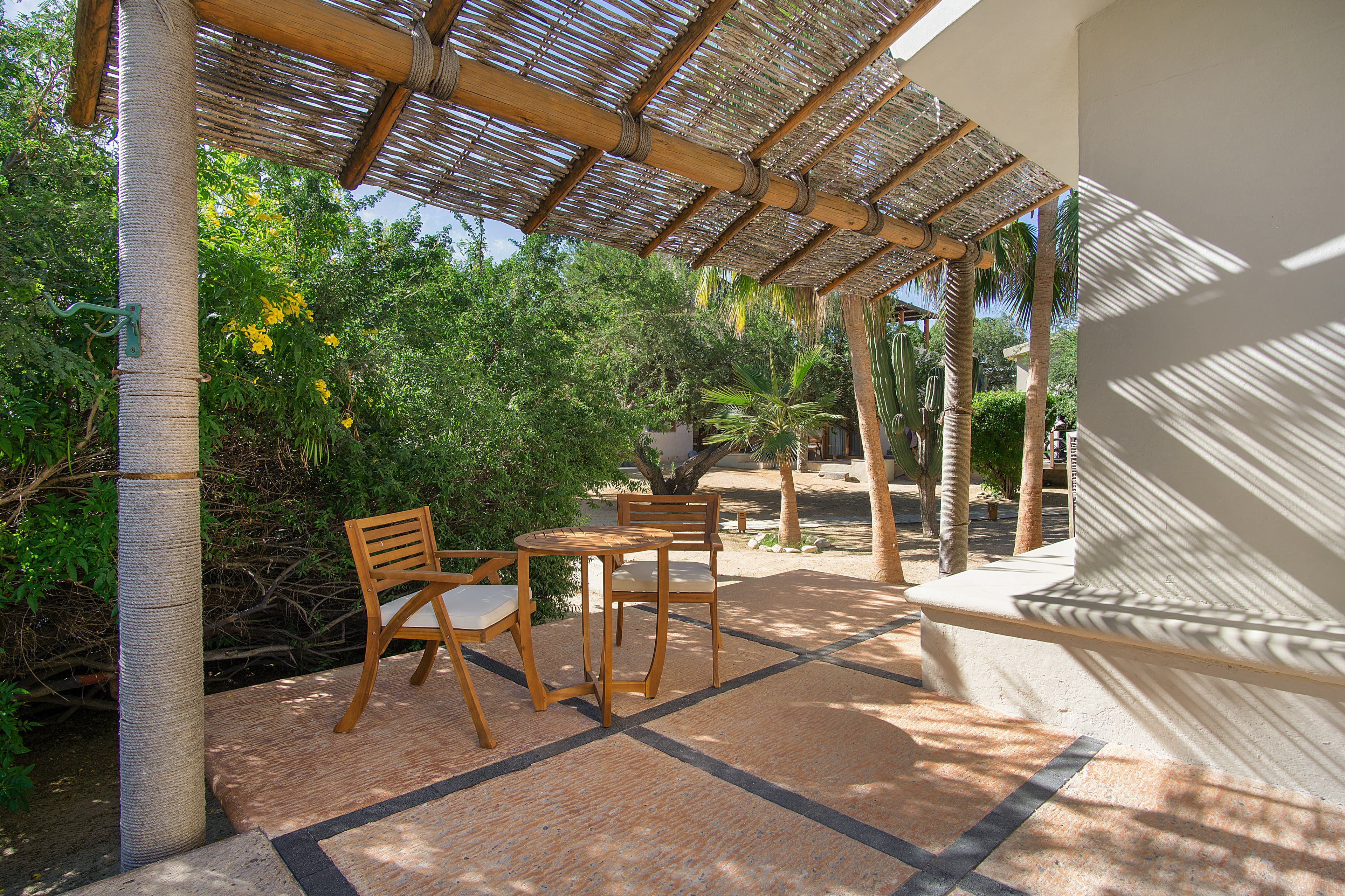 A shaded outdoor seating area with a table and chairs surrounded by greenery.