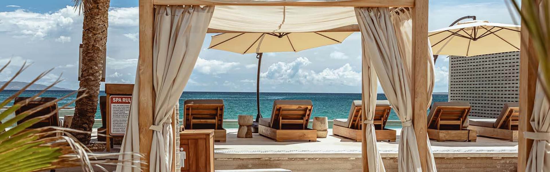 A serene beach cabana with lounge chairs and umbrellas overlooking the ocean.