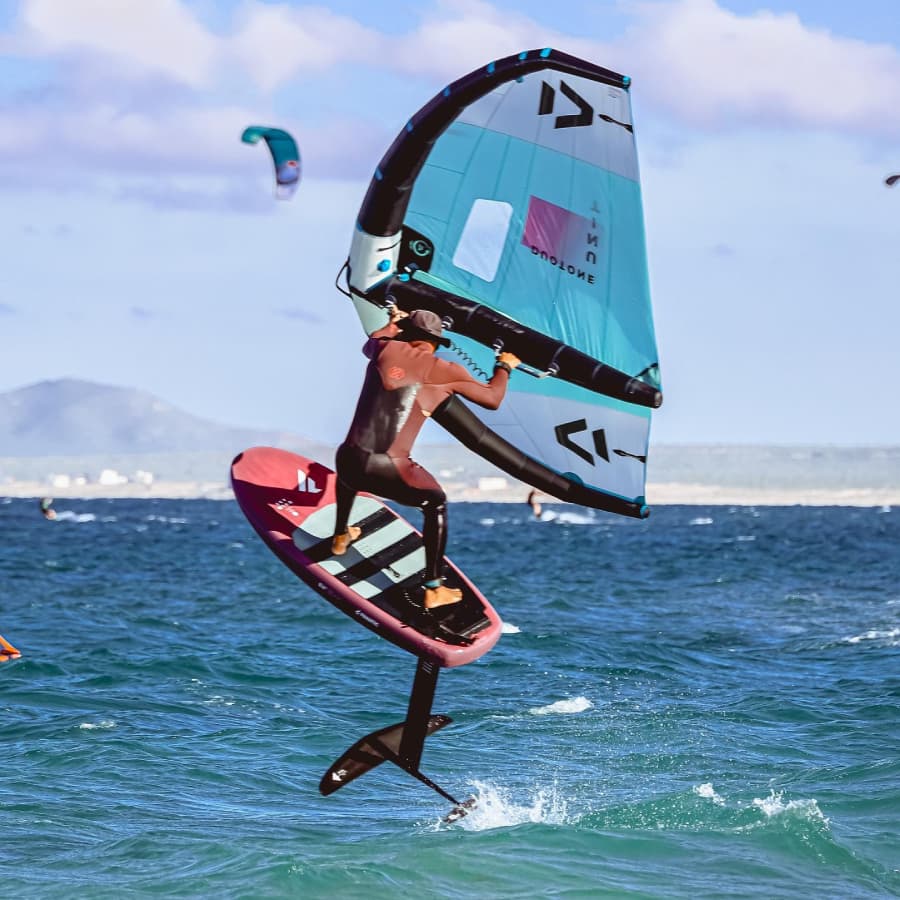 A person in a wetsuit is performing a maneuver while foiling on the water with a sail.