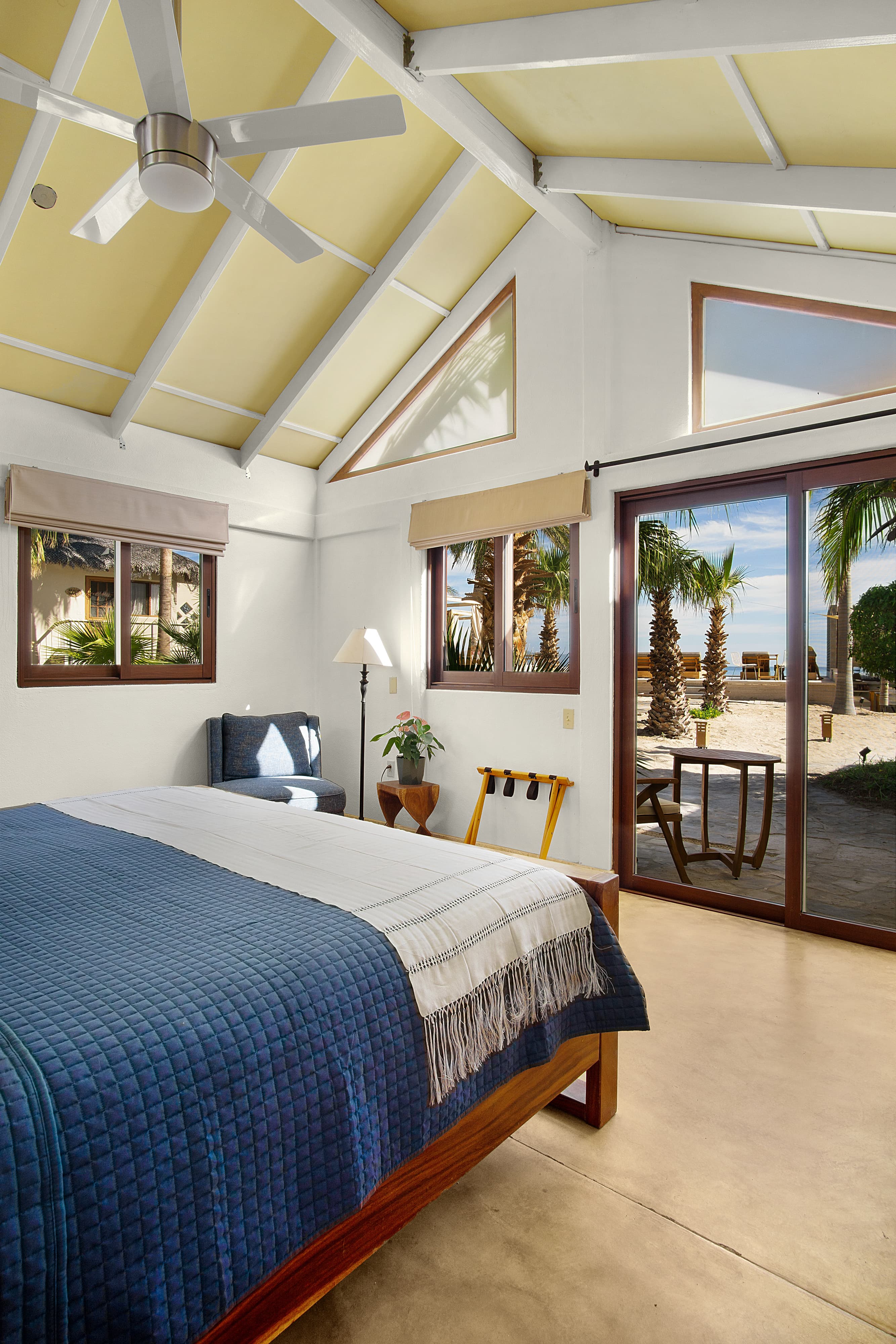 Bright, airy bedroom featuring a large window with views of palm trees and outdoor seating.