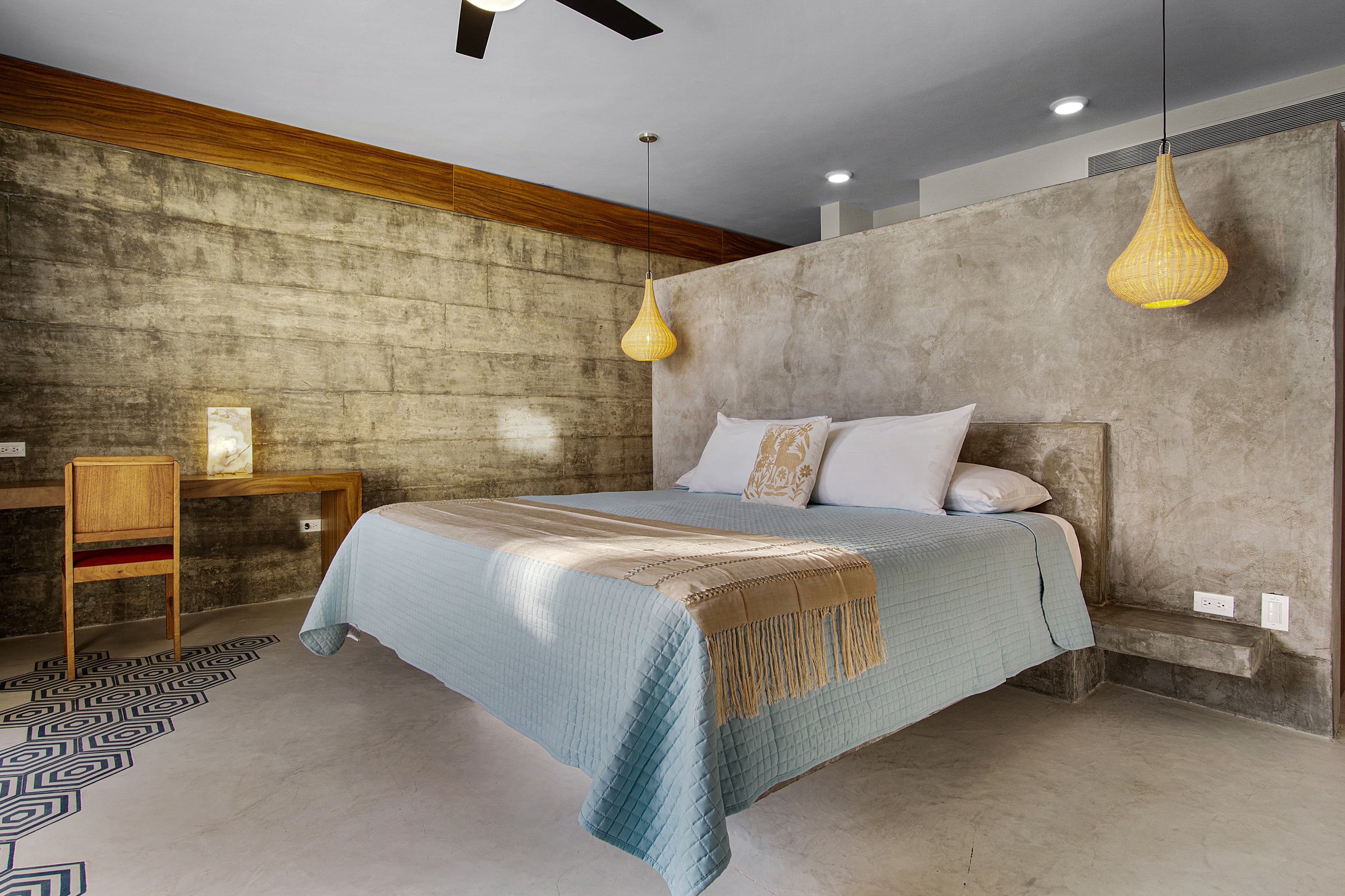 A modern bedroom featuring a concrete wall, a large bed with light blue bedding, and pendant lamps.