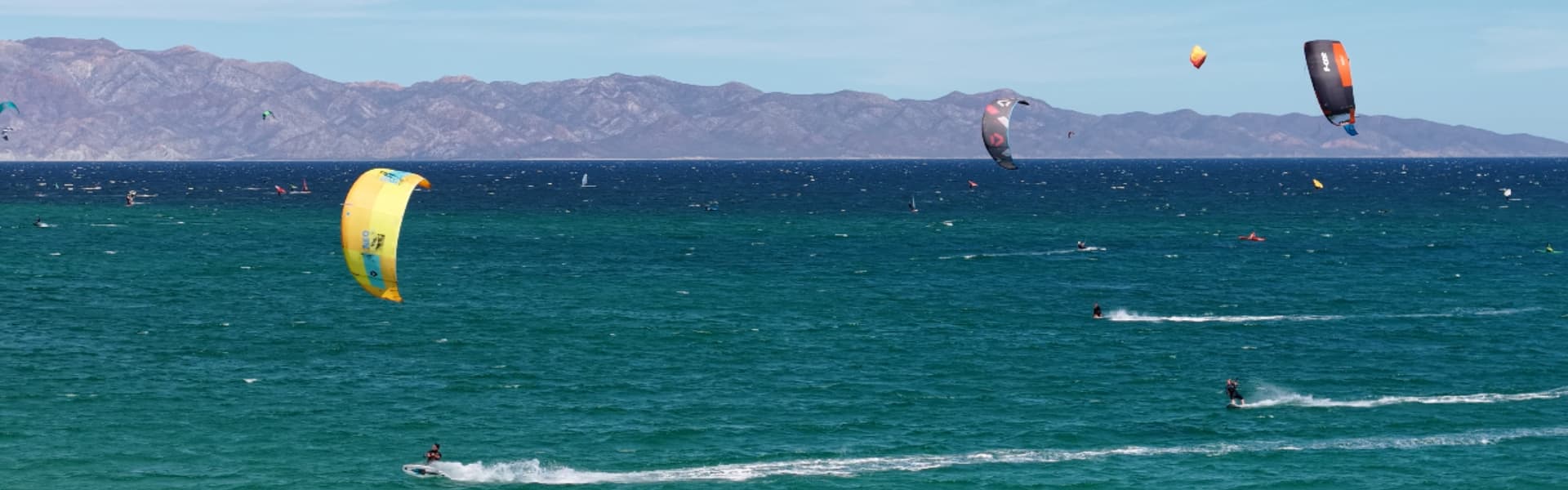 Kitesurfers navigate turquoise waters with mountains in the background.