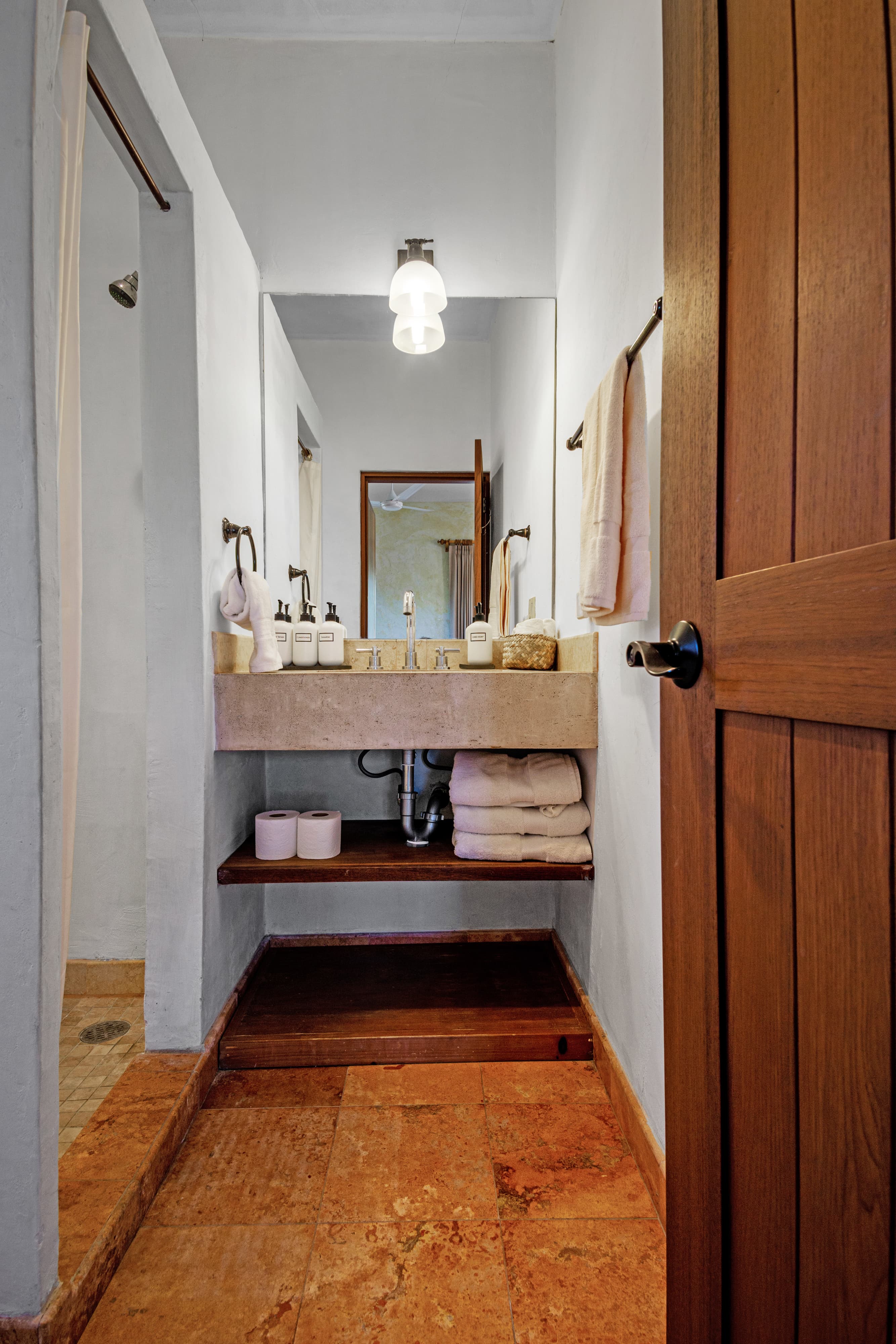 A modern bathroom featuring a stone sink, shelves with towels, and a wooden door.