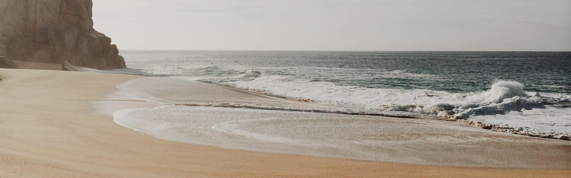 A serene beach scene with gentle waves and a rocky cliff.