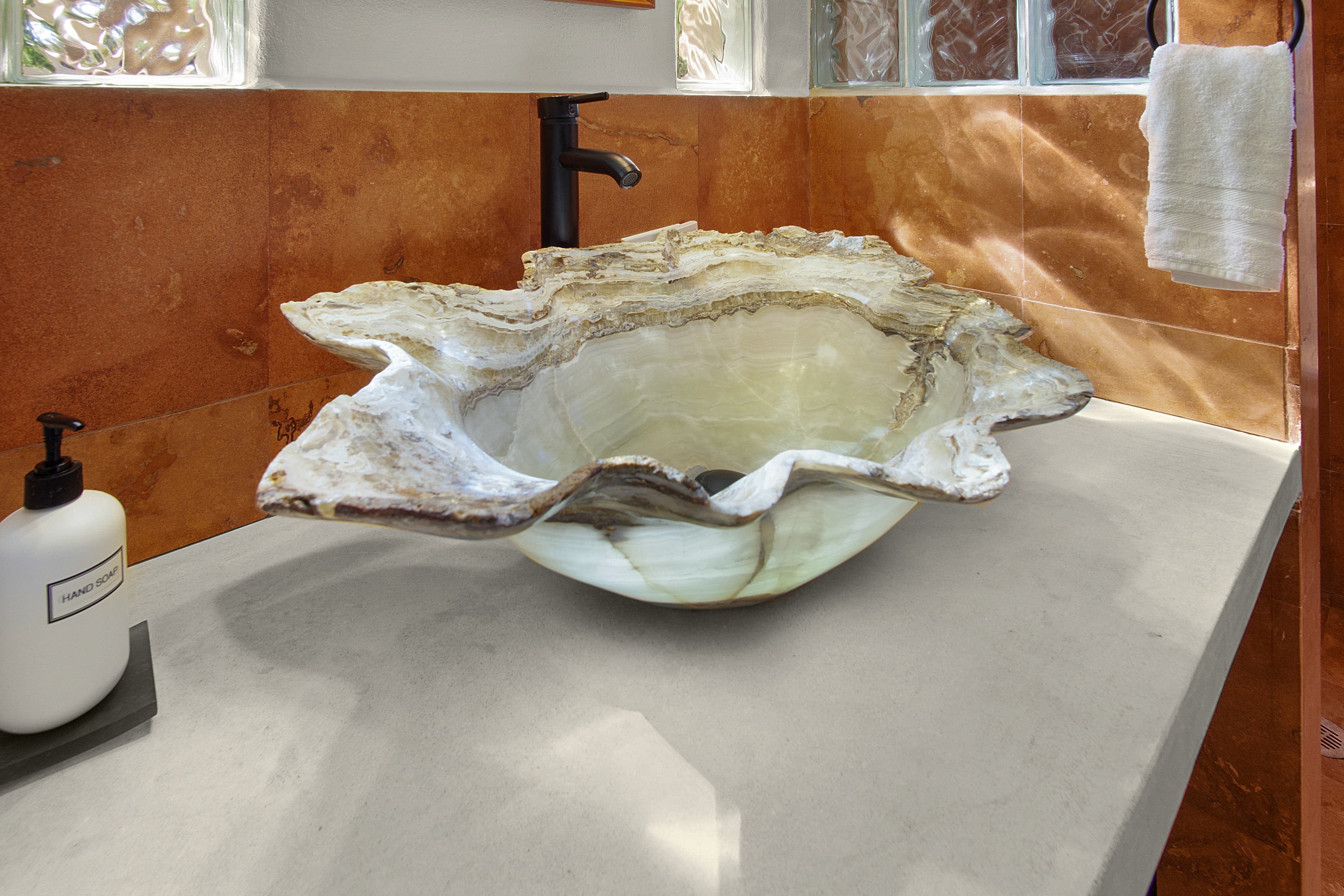 A decorative, shell-shaped sink made of stone sits on a smooth countertop in a bathroom setting.