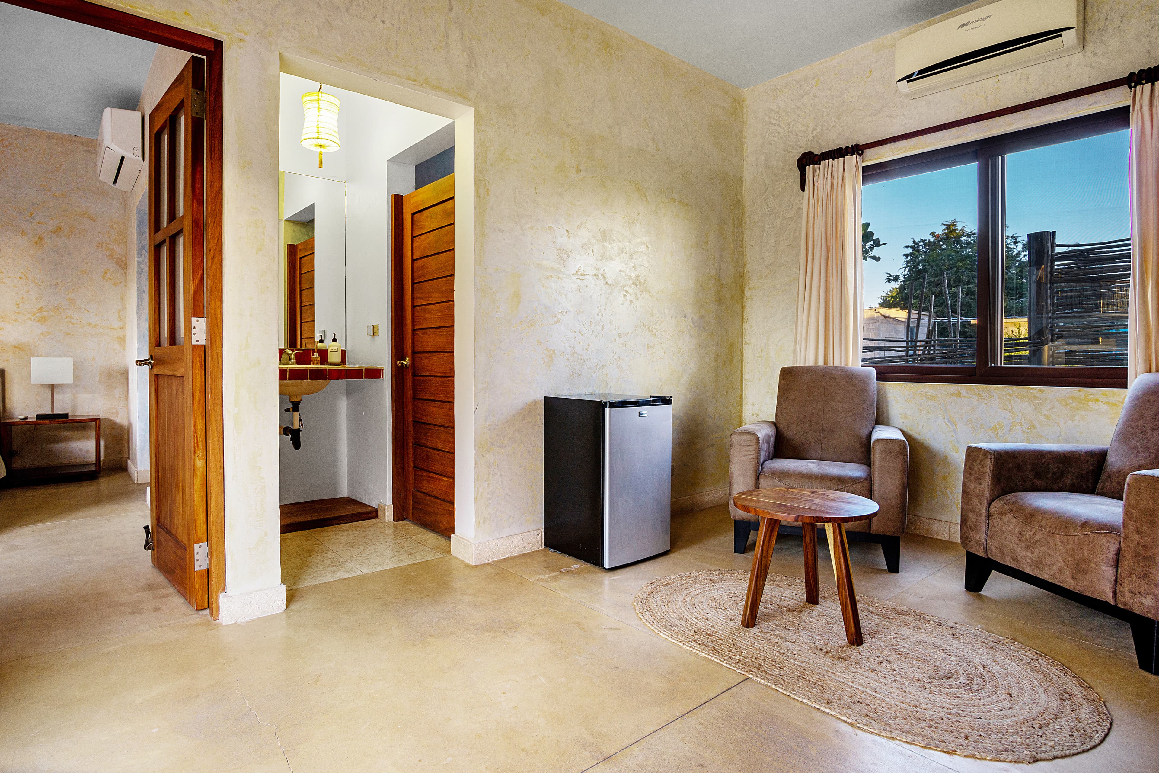 A cozy room featuring two armchairs, a small table, a mini fridge, and a doorway leading to a bathroom.