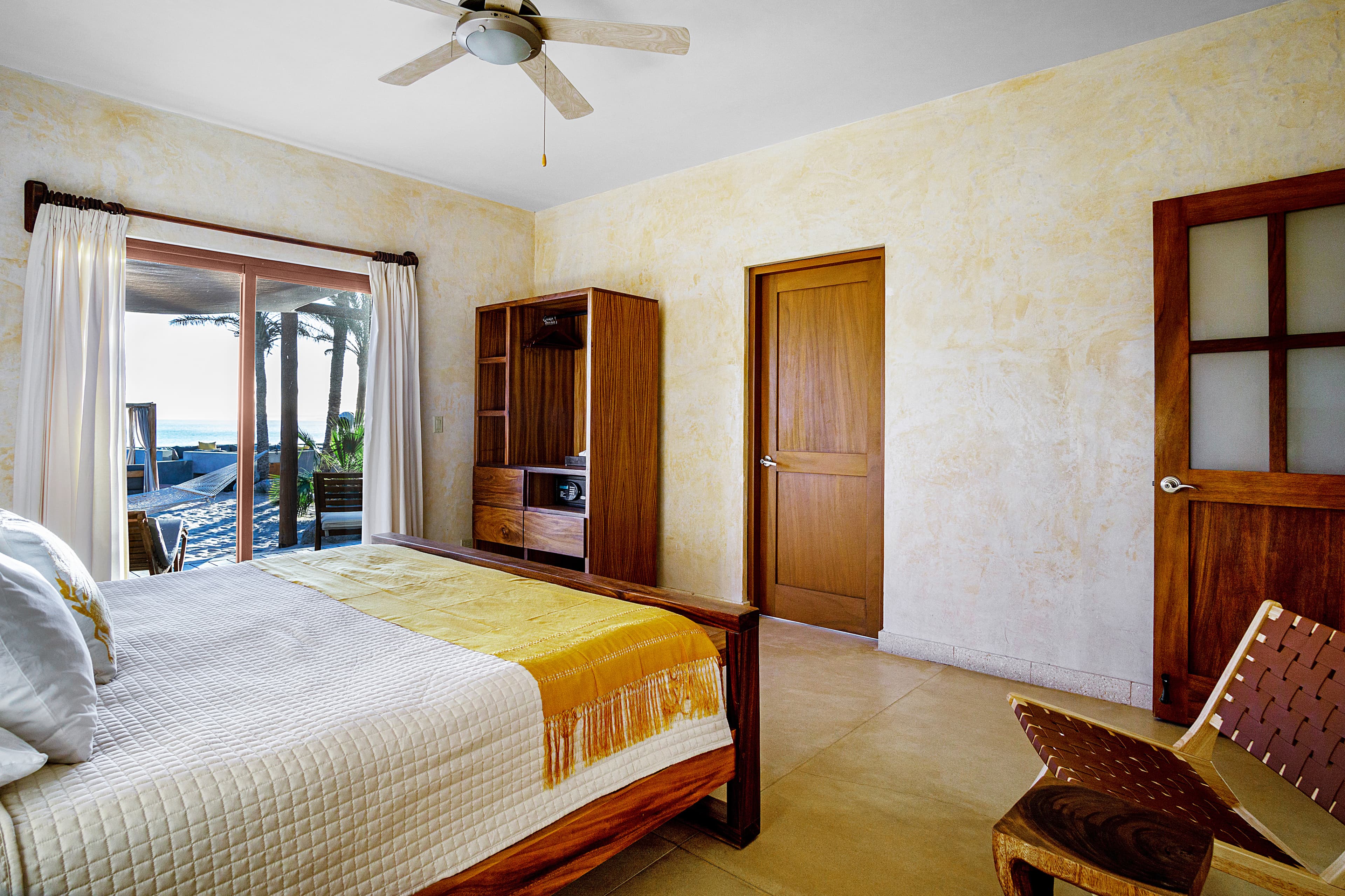 A cozy bedroom featuring a wooden bed, a small dresser, and a view through large glass doors.