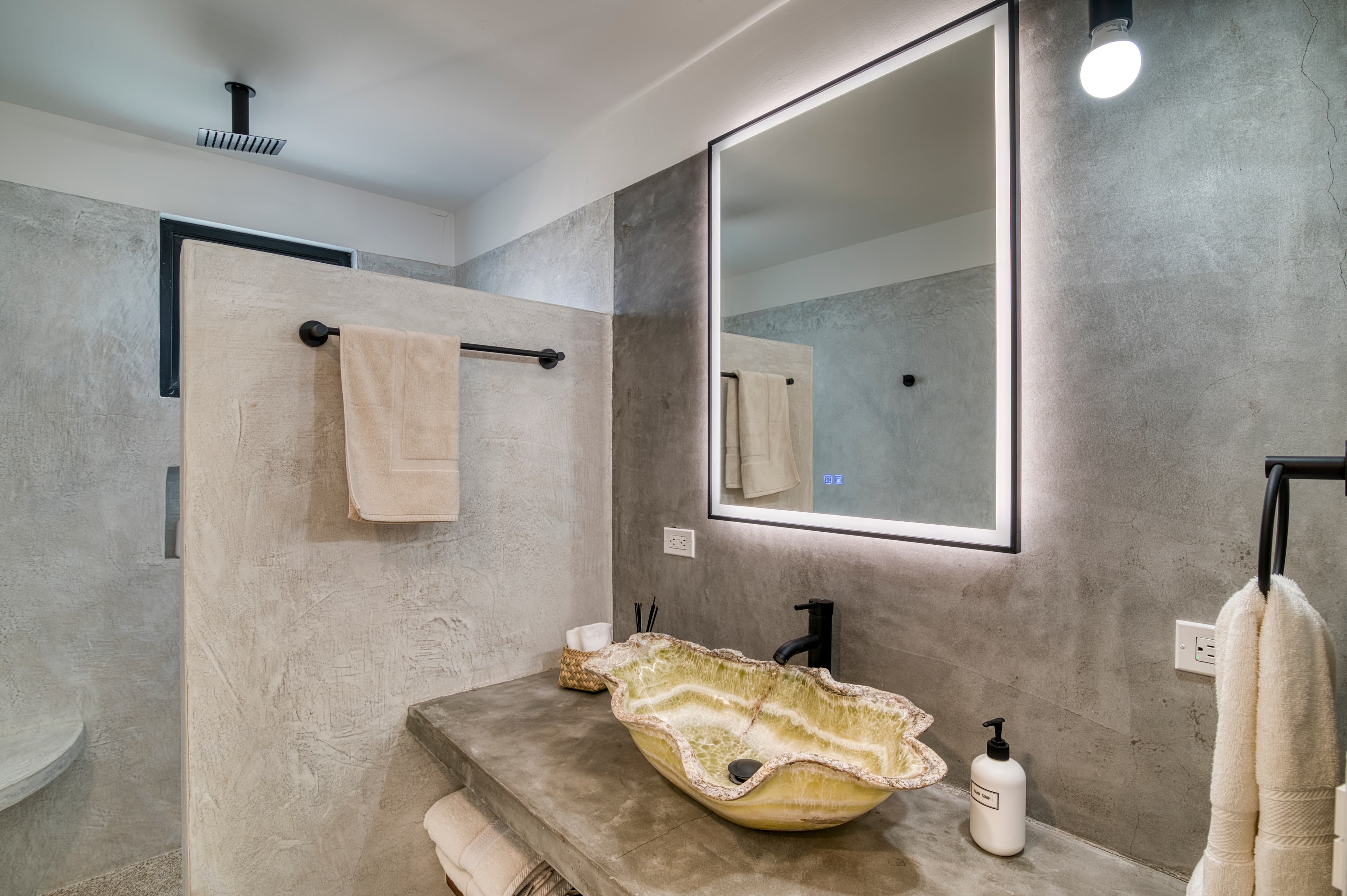 Modern bathroom with a concrete sink, decorative shell basin, and illuminated mirror.