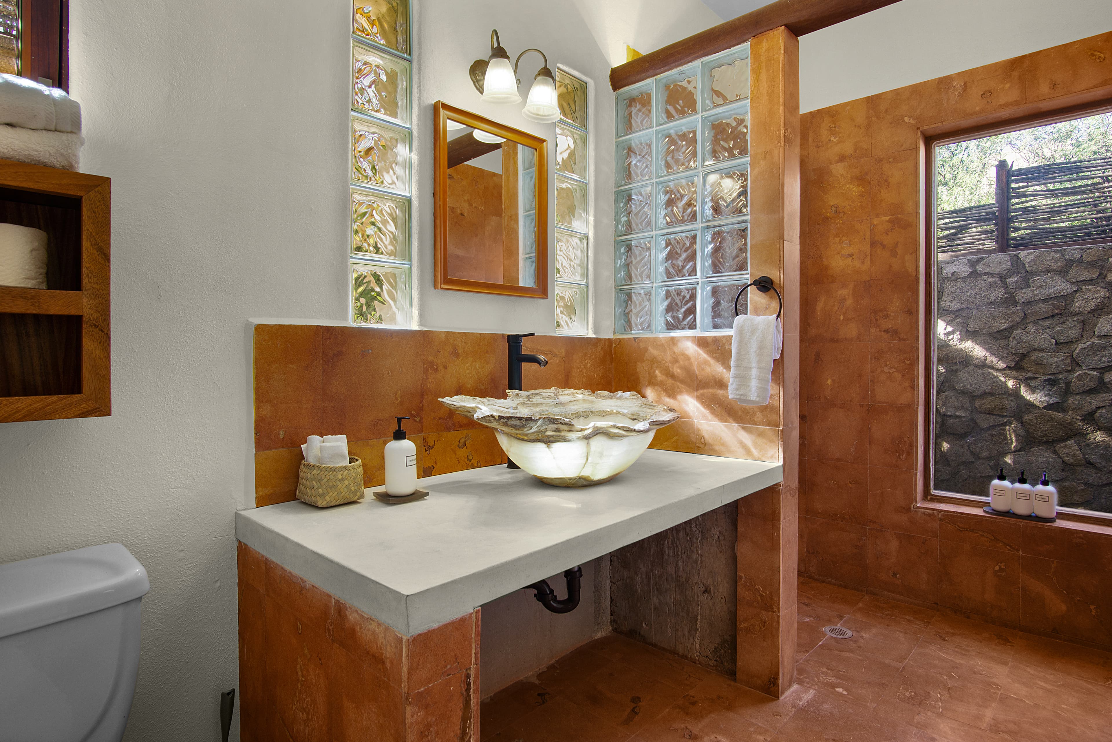 A modern bathroom featuring a stone sink, wooden accents, and natural light from large windows.