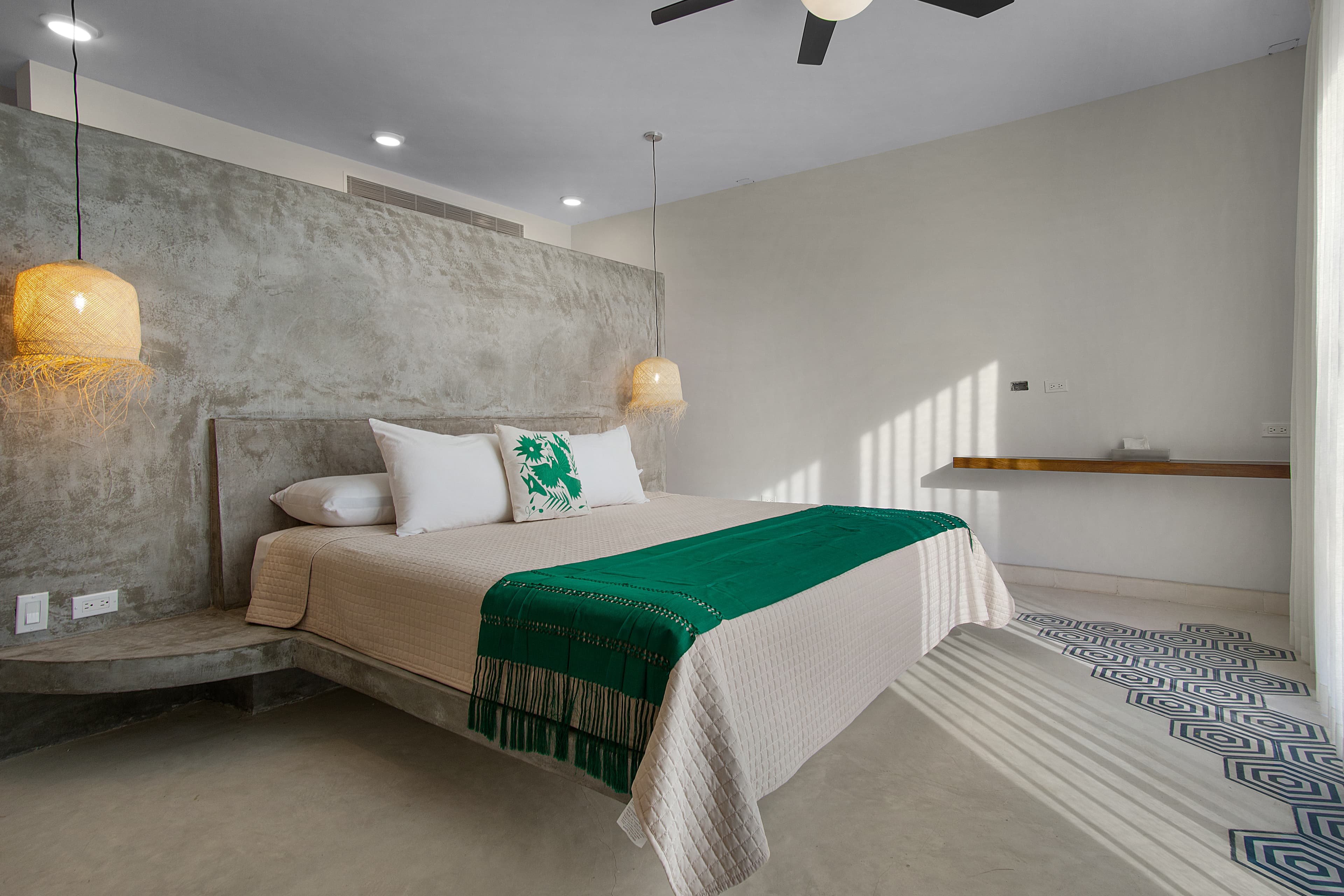 A modern bedroom with a concrete wall, a large bed featuring a green throw, and subtle lighting.