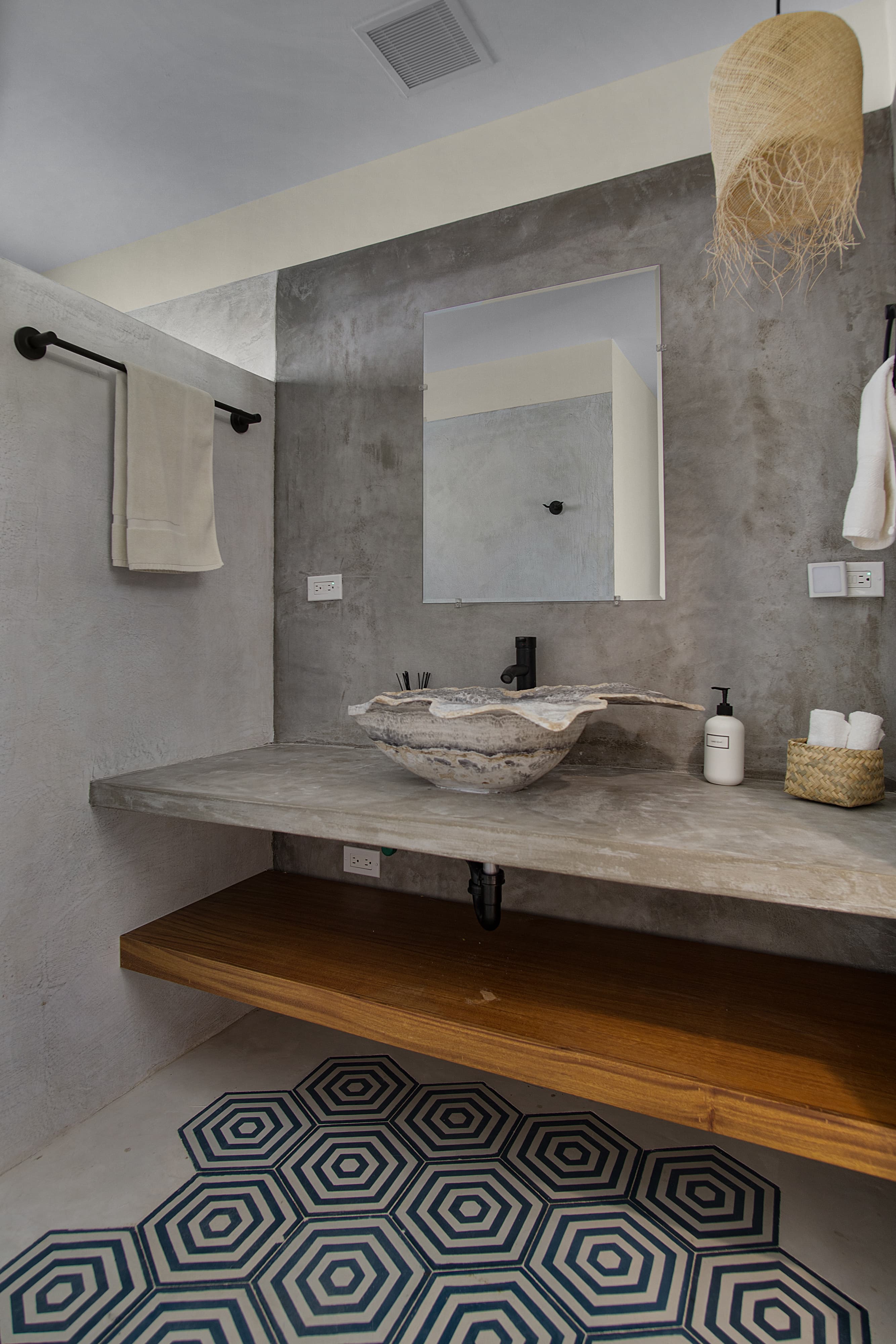 Modern bathroom featuring a concrete sink, large mirror, and hexagonal patterned rug.