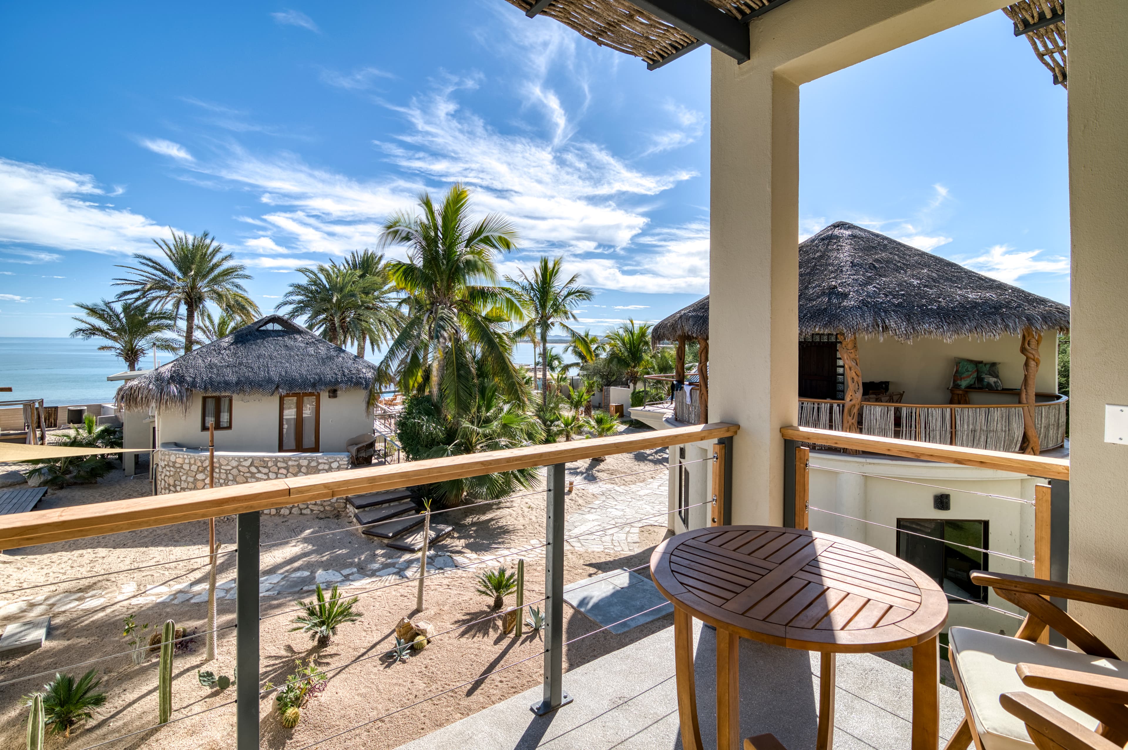 A balcony view overlooking a tropical landscape with palms and thatched huts by the beach.