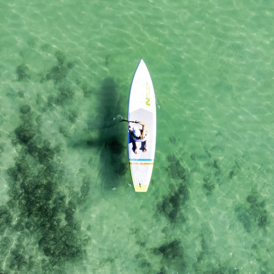 A person paddles on a stand-up paddleboard in clear turquoise water.