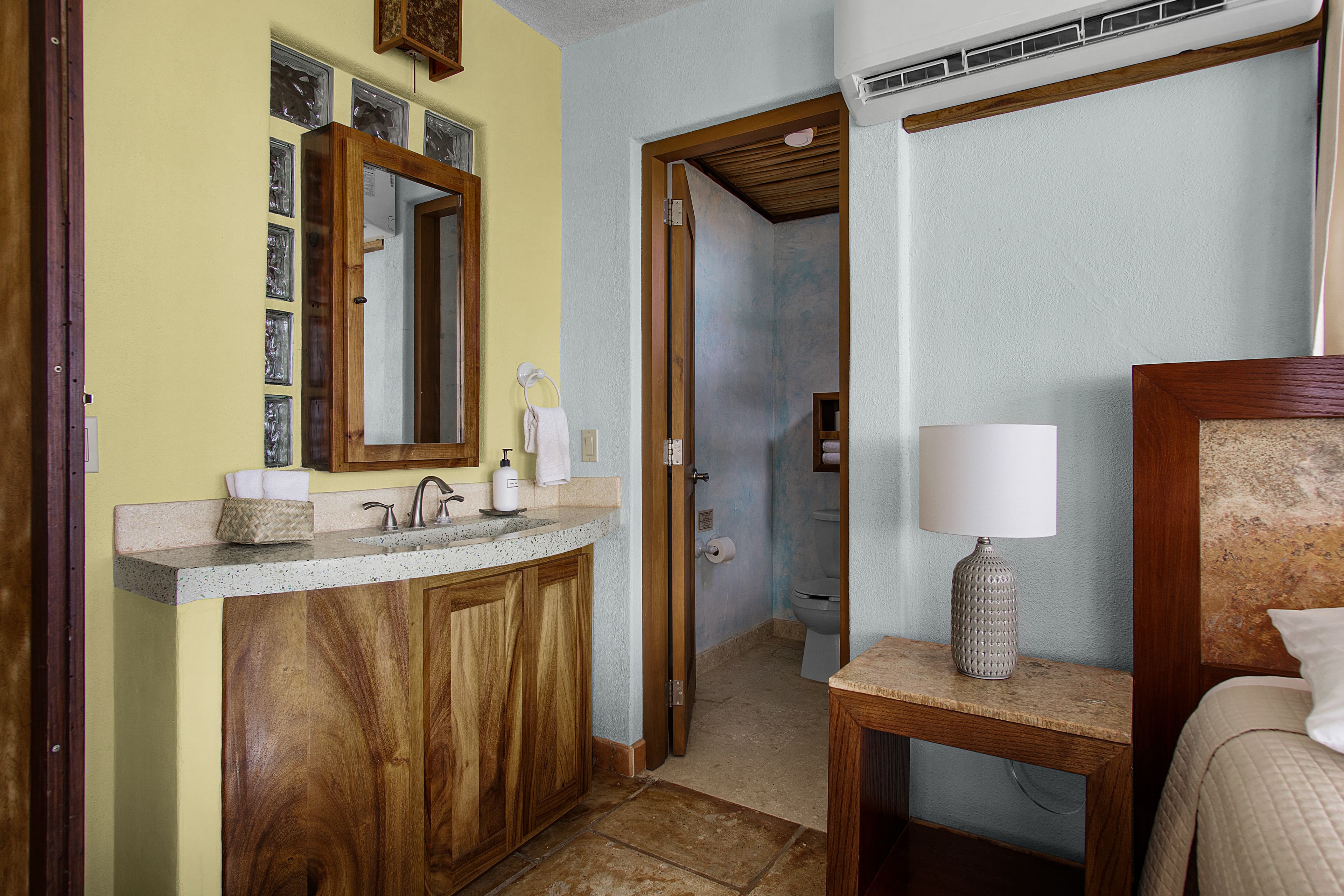 A modern bathroom with a wooden vanity, mirror, and a doorway leading to a separate toilet area.