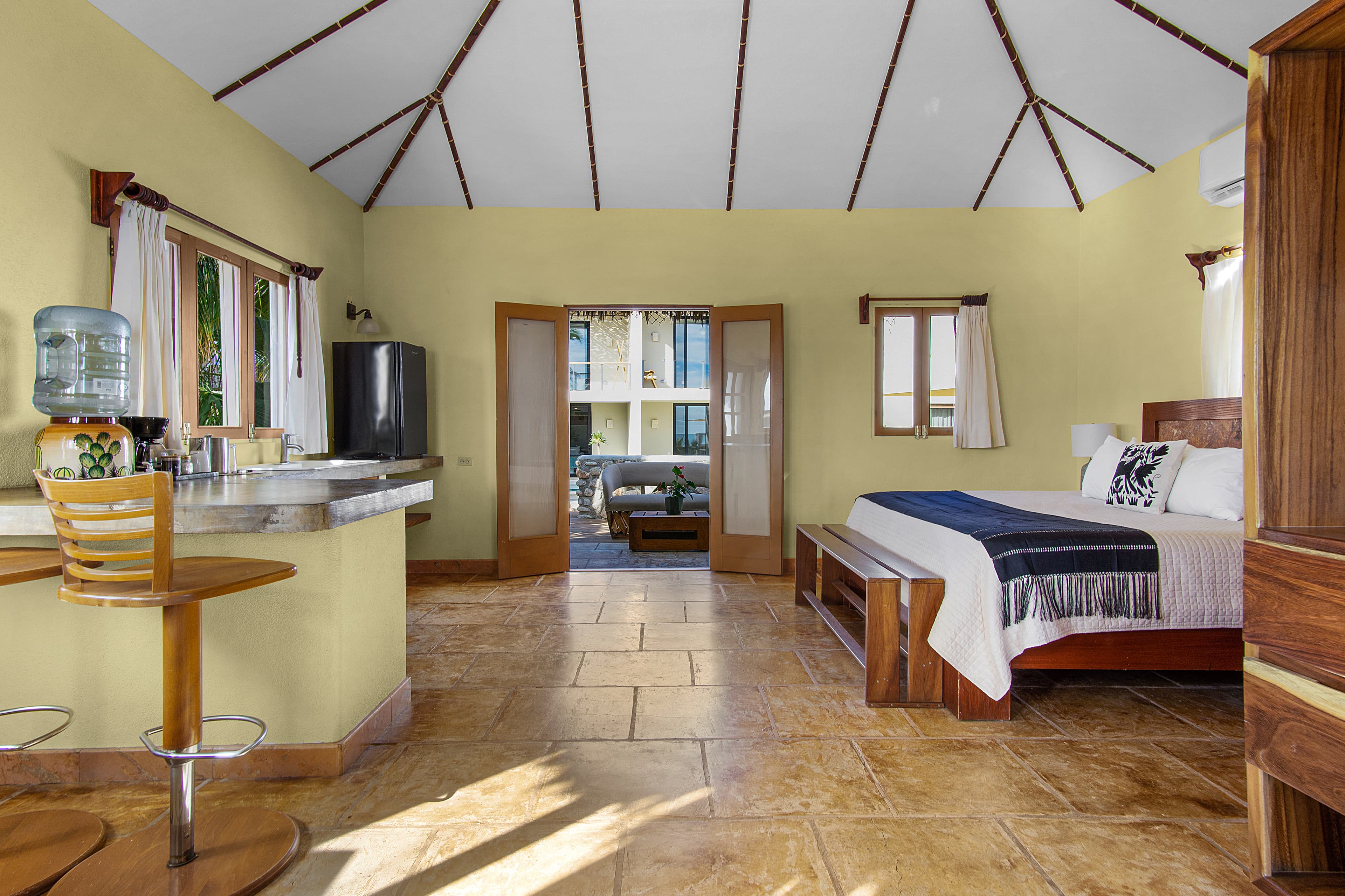 Bright, airy hotel room with a kitchenette and doors opening to an outdoor seating area.