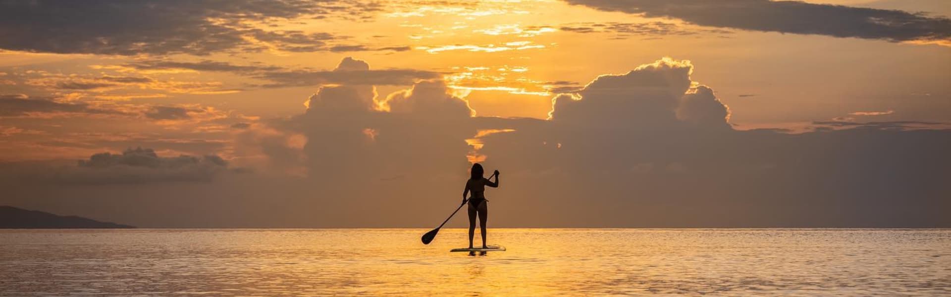 A silhouette of a person paddleboarding at sunset over calm waters.