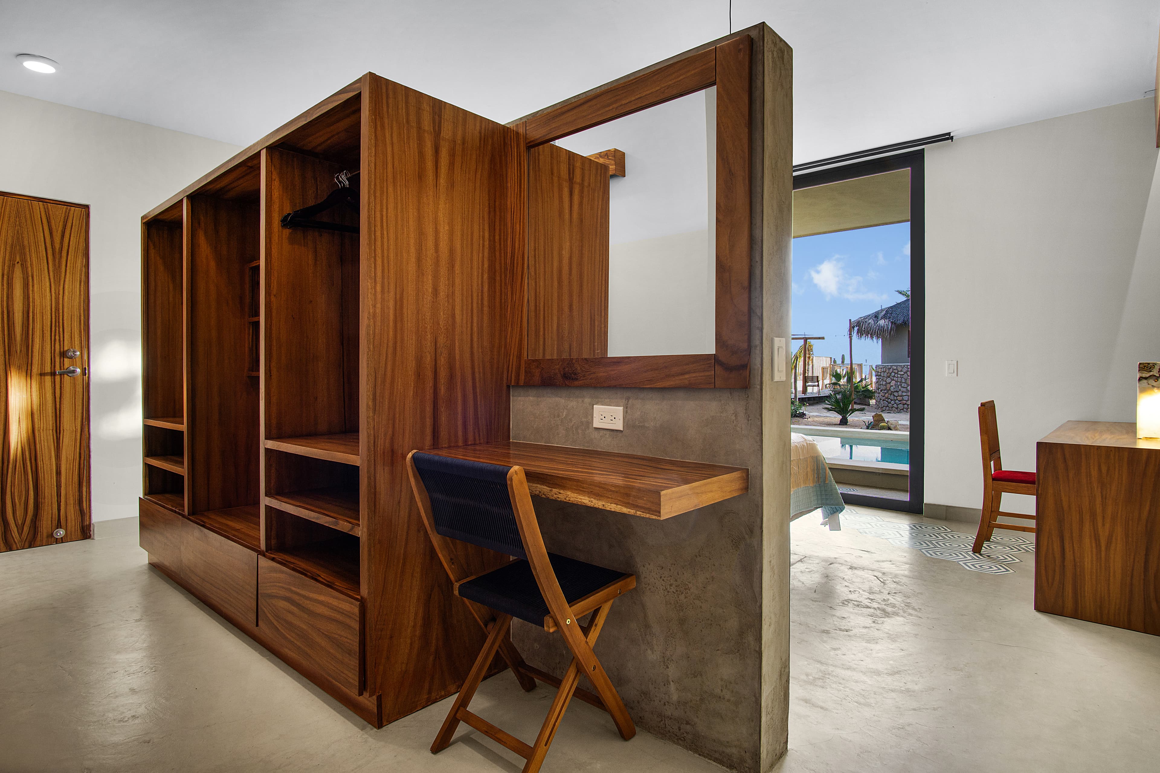 A modern bedroom featuring a wooden wardrobe, a small desk, and large windows overlooking an outdoor space.