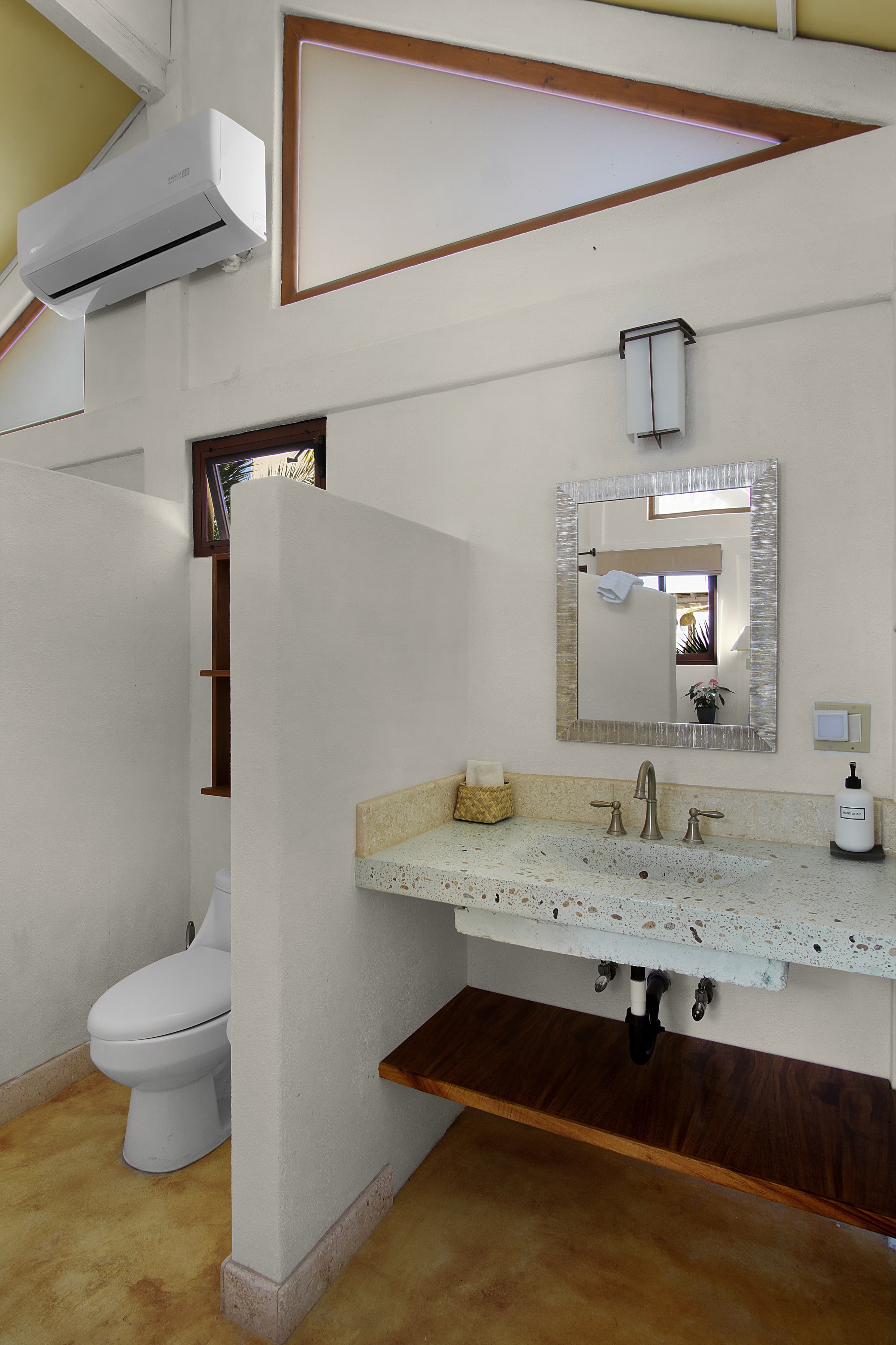 A modern bathroom featuring a toilet, a stylish sink with a speckled countertop, a large mirror, and natural light.