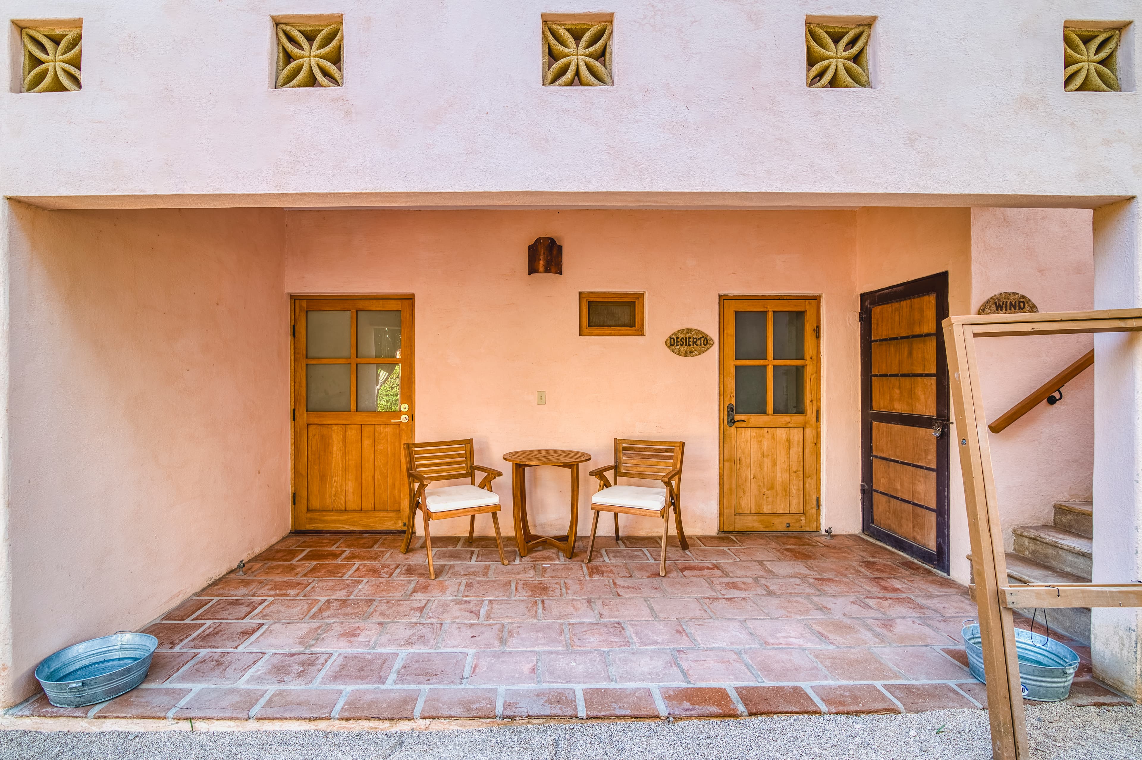 A cozy entrance with two wooden chairs and a table under a pink wall, featuring doors to adjacent rooms.