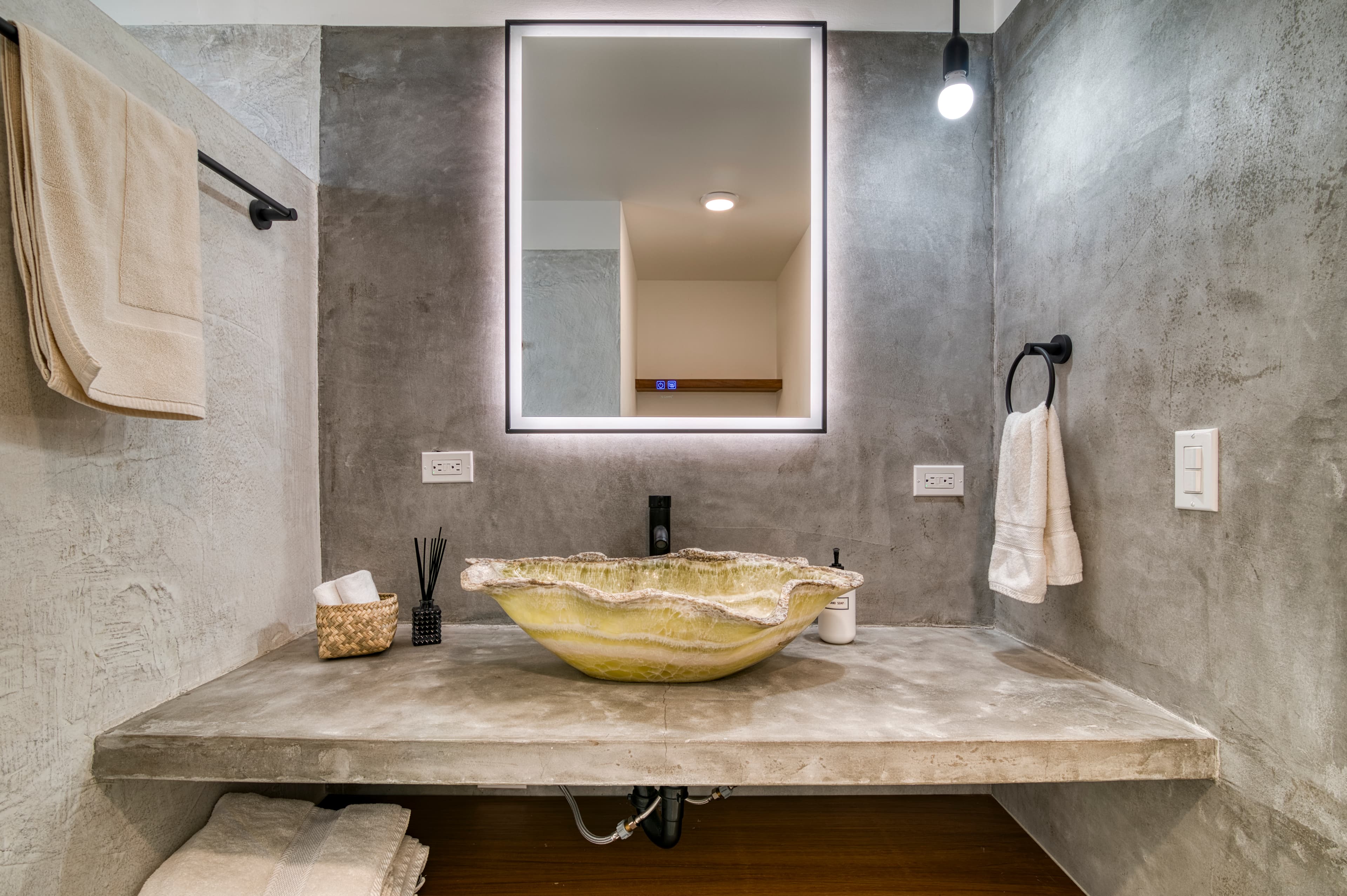Modern bathroom featuring a concrete sink, illuminated mirror, and stylish accessories.
