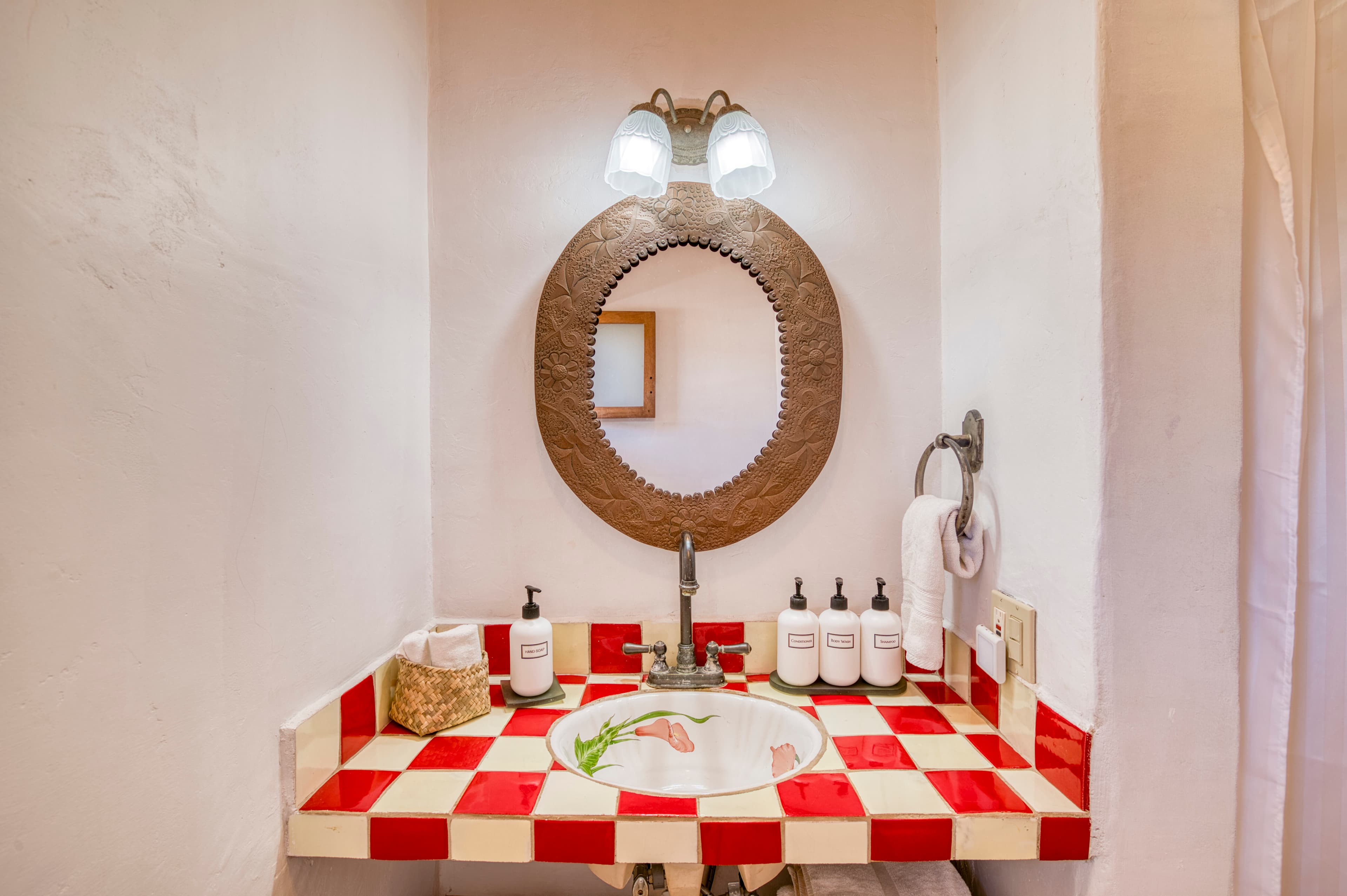 A vibrant bathroom featuring a red and white checkered countertop, a round wooden mirror, and stylish toiletries.