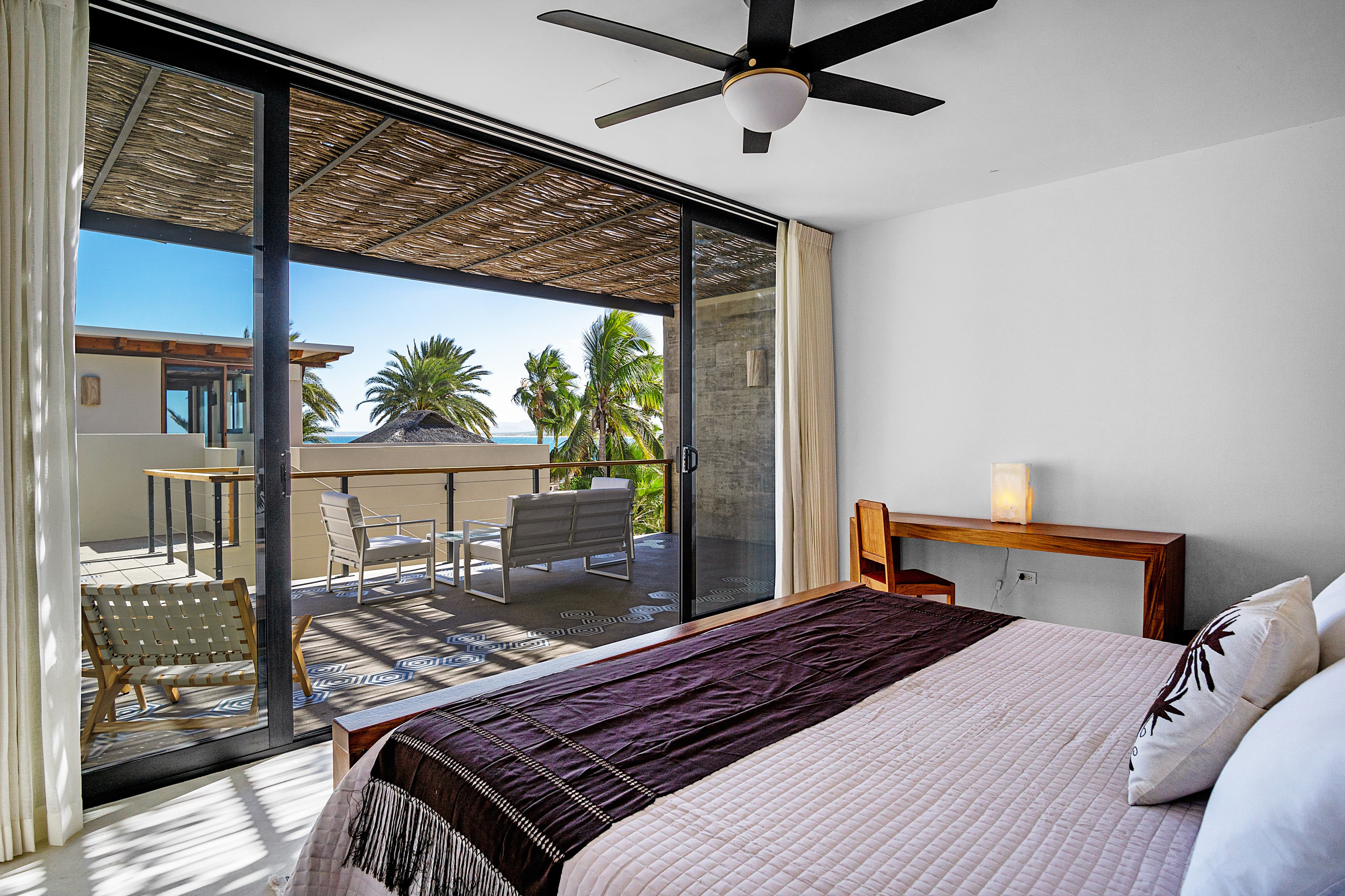 A modern bedroom with a view of a balcony and palm trees outside.