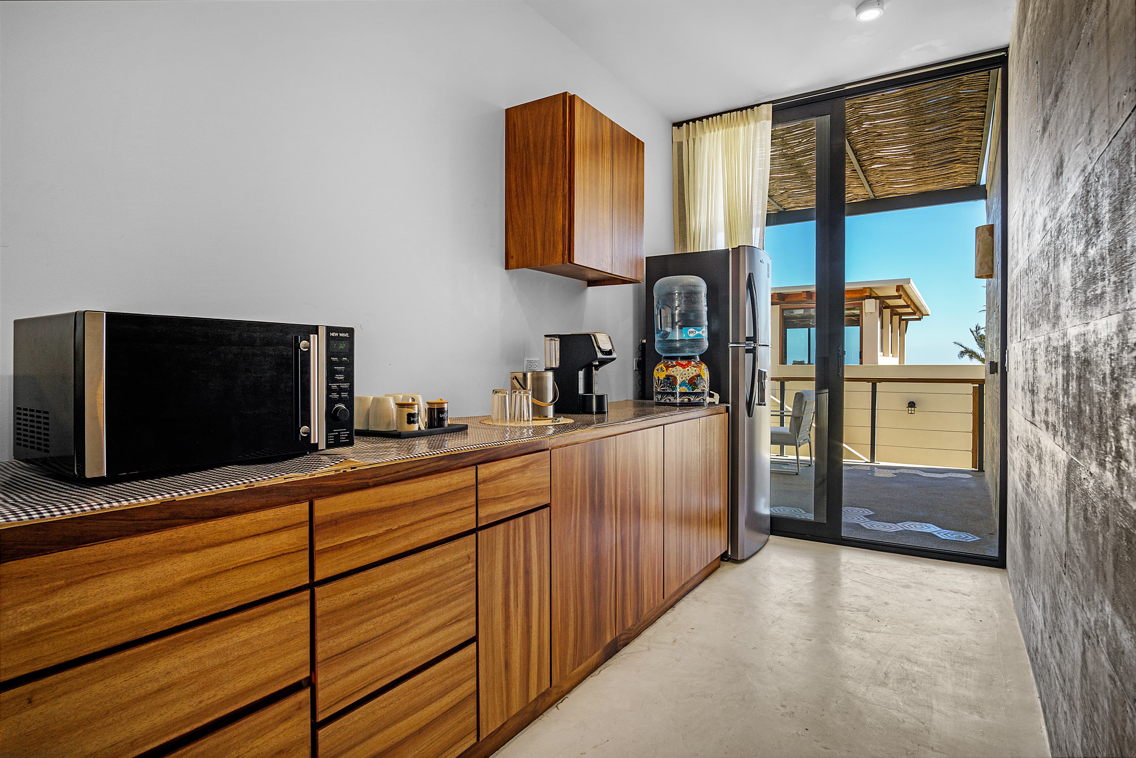Modern kitchen with wooden cabinetry, microwave, coffee maker, and water dispenser, featuring large glass doors leading to an outdoor area.