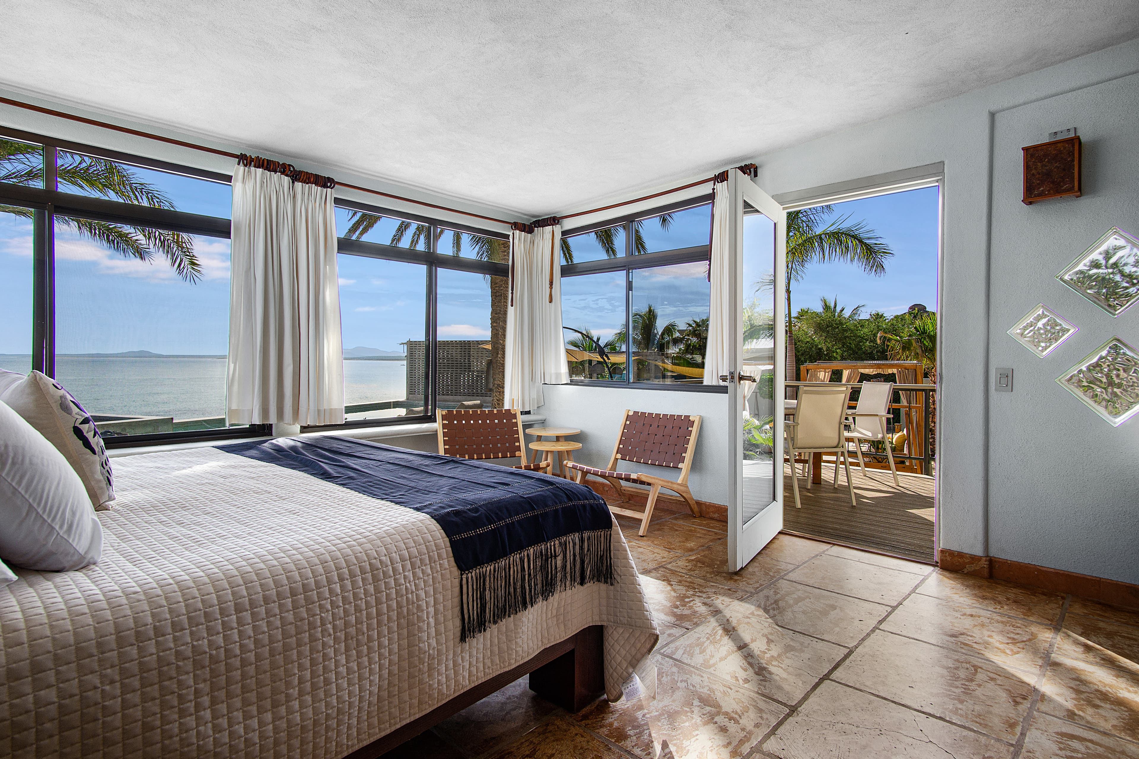 Cozy bedroom with large windows showcasing a beach view and access to a deck with outdoor seating.