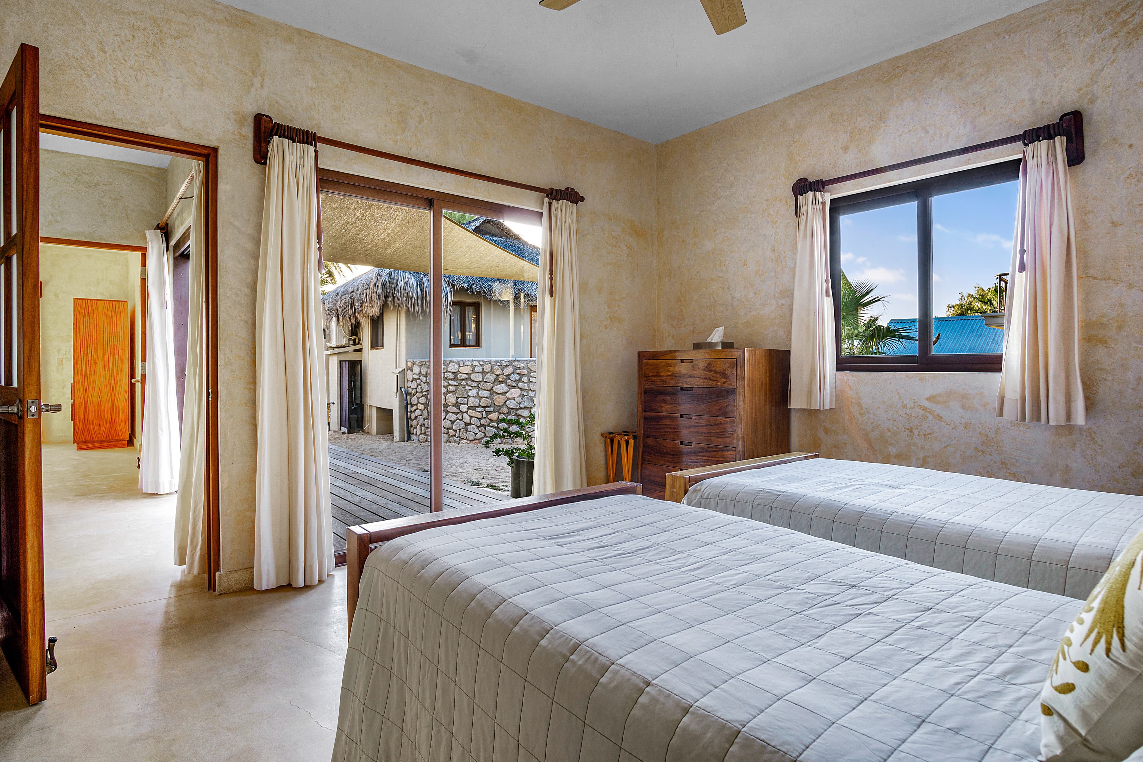A cozy bedroom featuring two twin beds, with large windows showing an outdoor view.
