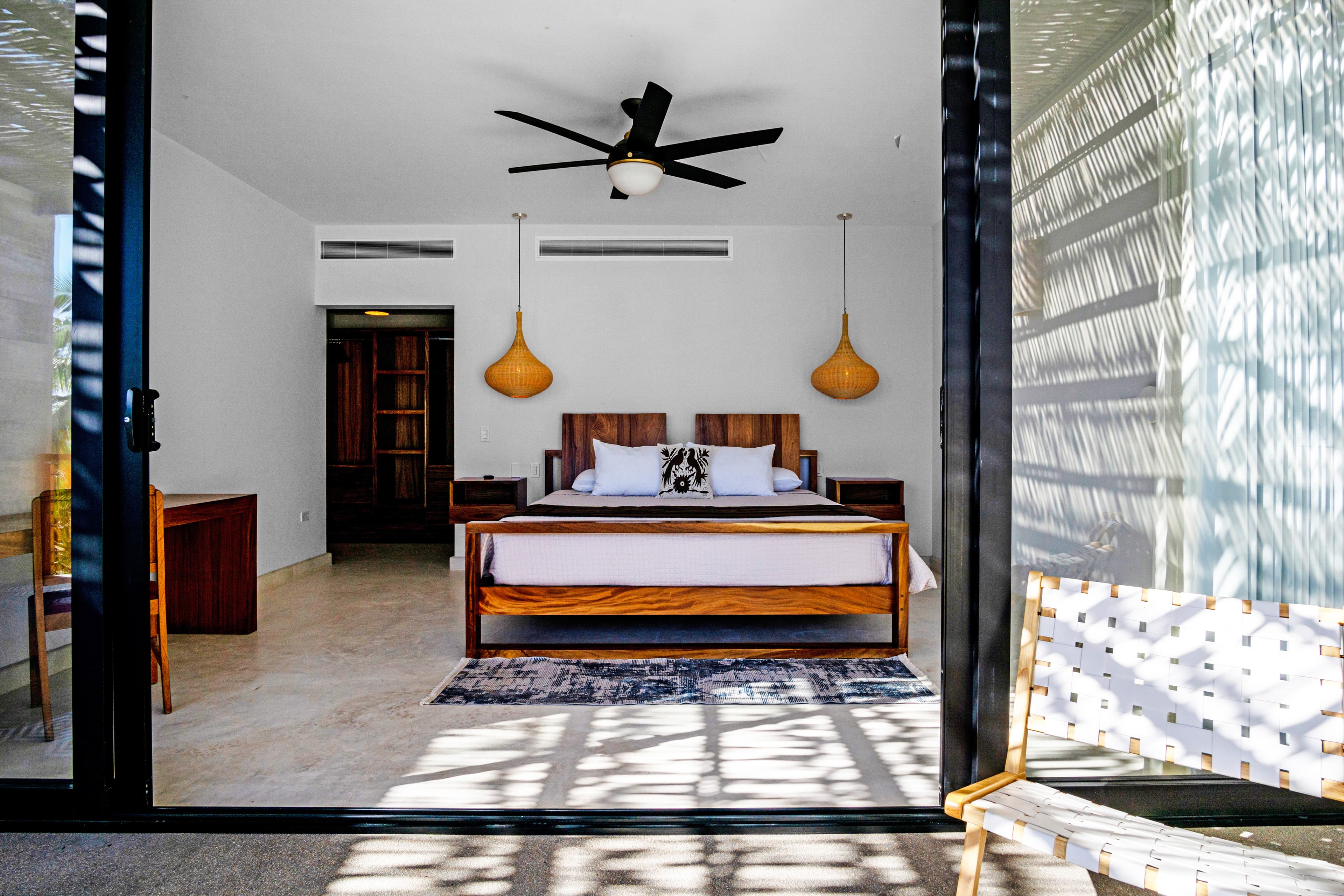 A modern bedroom with a wooden bed, decorative pillows, a ceiling fan, and large sliding glass doors leading to an outdoor patio.