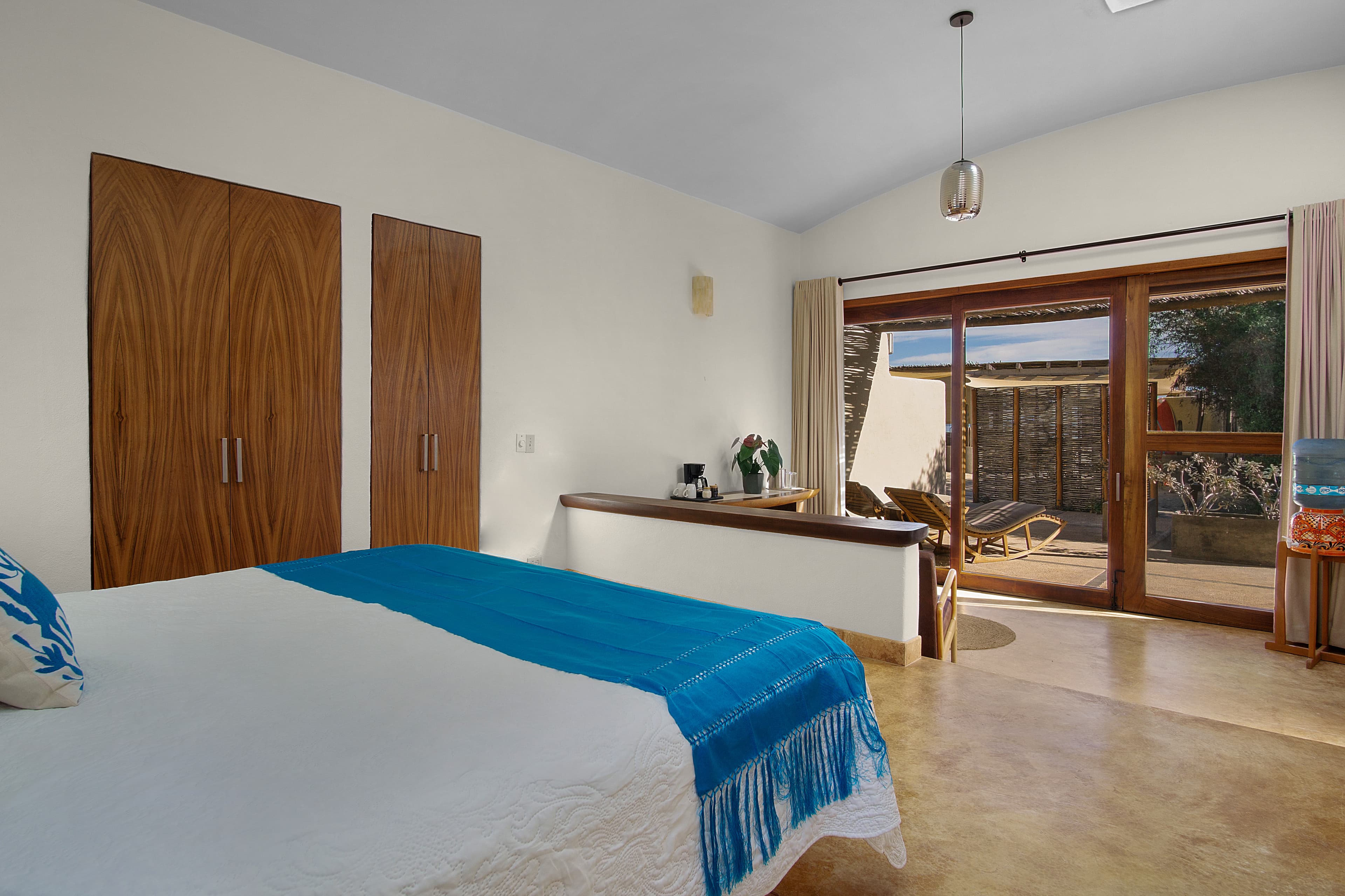 A spacious, modern bedroom featuring a bed with blue linens and large glass doors opening to a courtyard.