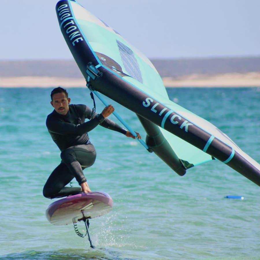A man in a wetsuit is performing a jump on a hydrofoil board while holding a large sail.