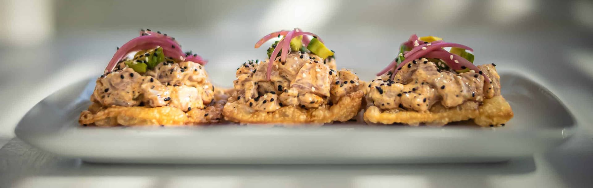 Three crispy tortillas topped with creamy tuna, pickled onions, and sesame seeds.