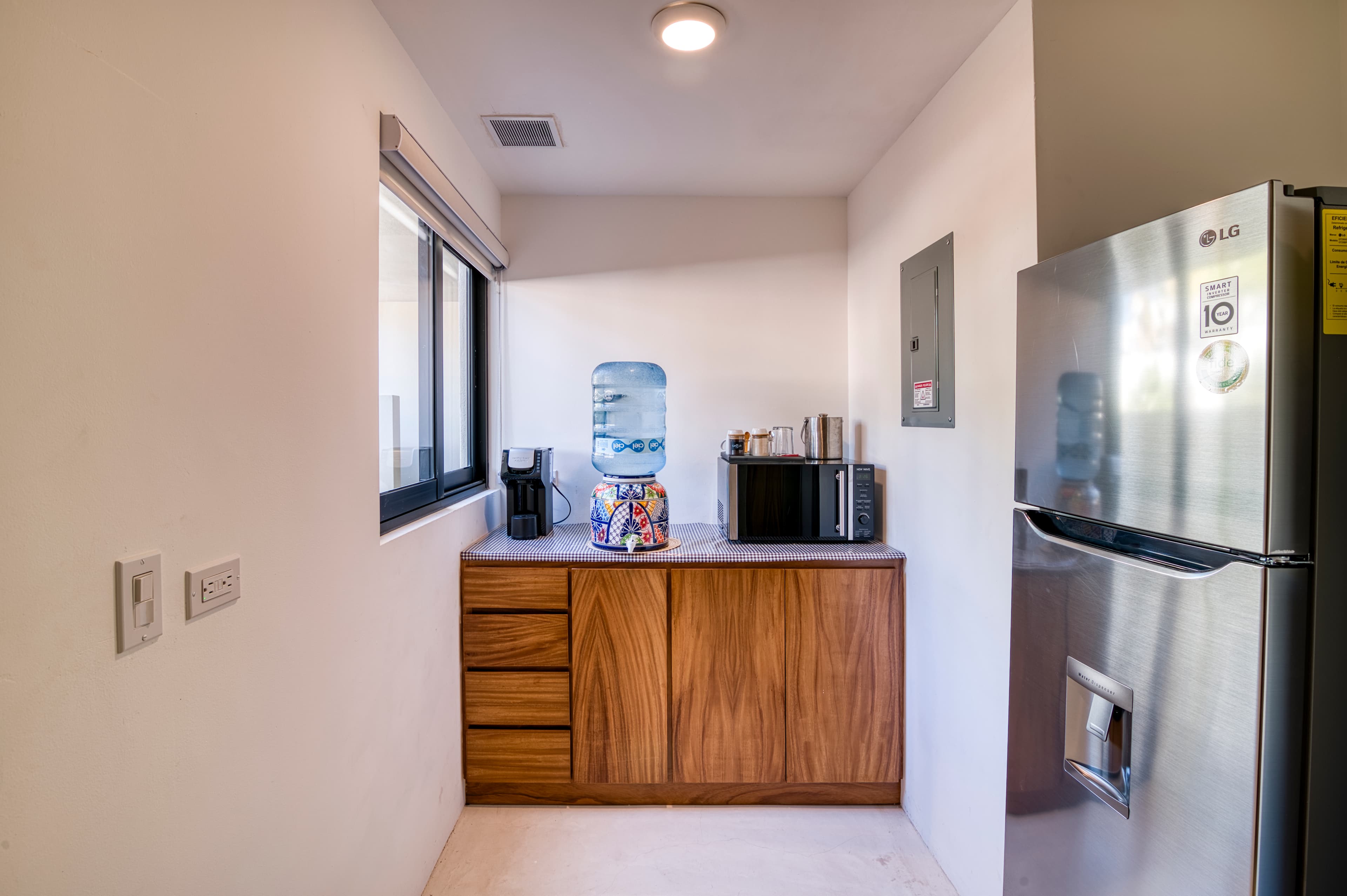 A modern kitchenette featuring a wooden cabinet, a water cooler, a microwave, and a stainless steel refrigerator.