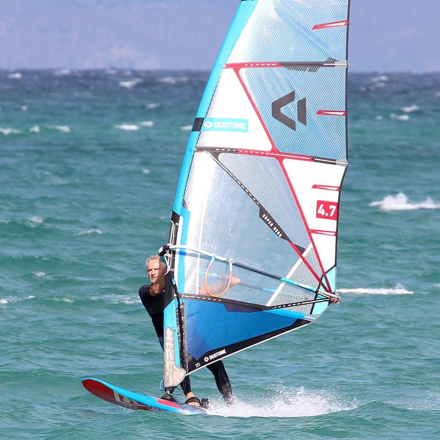 A windsurfer expertly navigates the waves on a blue and red board.