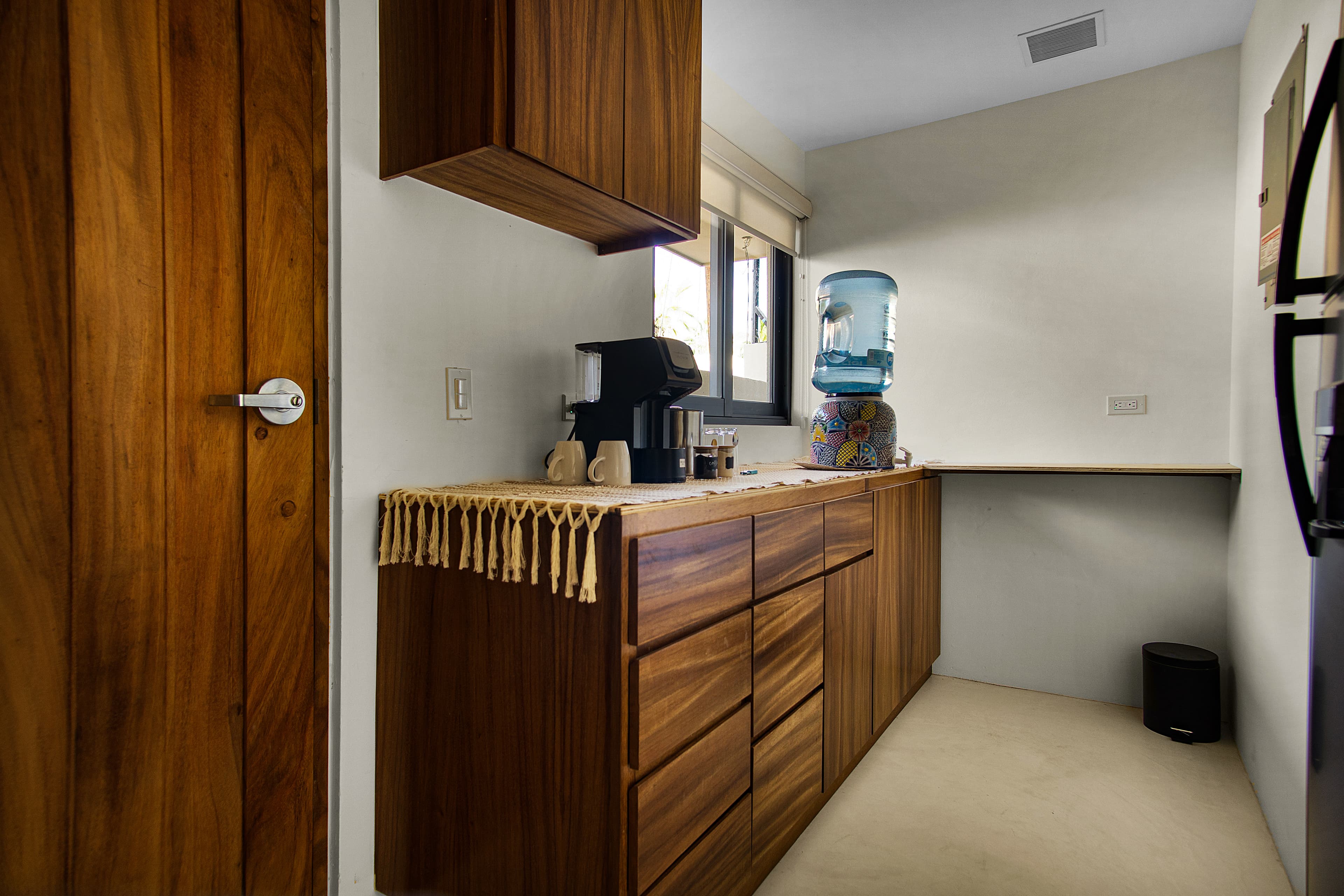 A modern kitchen with wooden cabinets, a coffee maker, and a water dispenser against a light-colored wall.