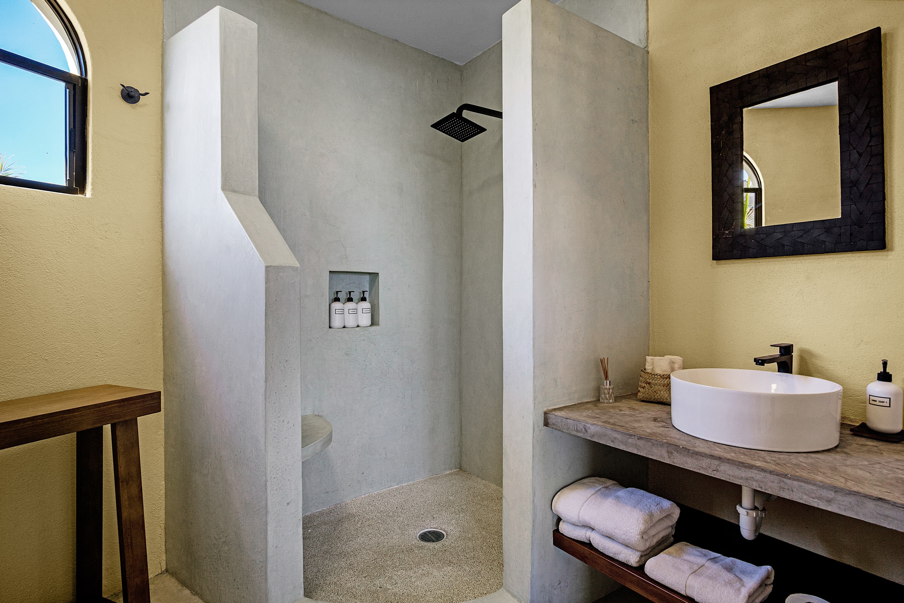 Modern bathroom featuring a shower with a concrete design, a round sink, and neatly arranged towels.