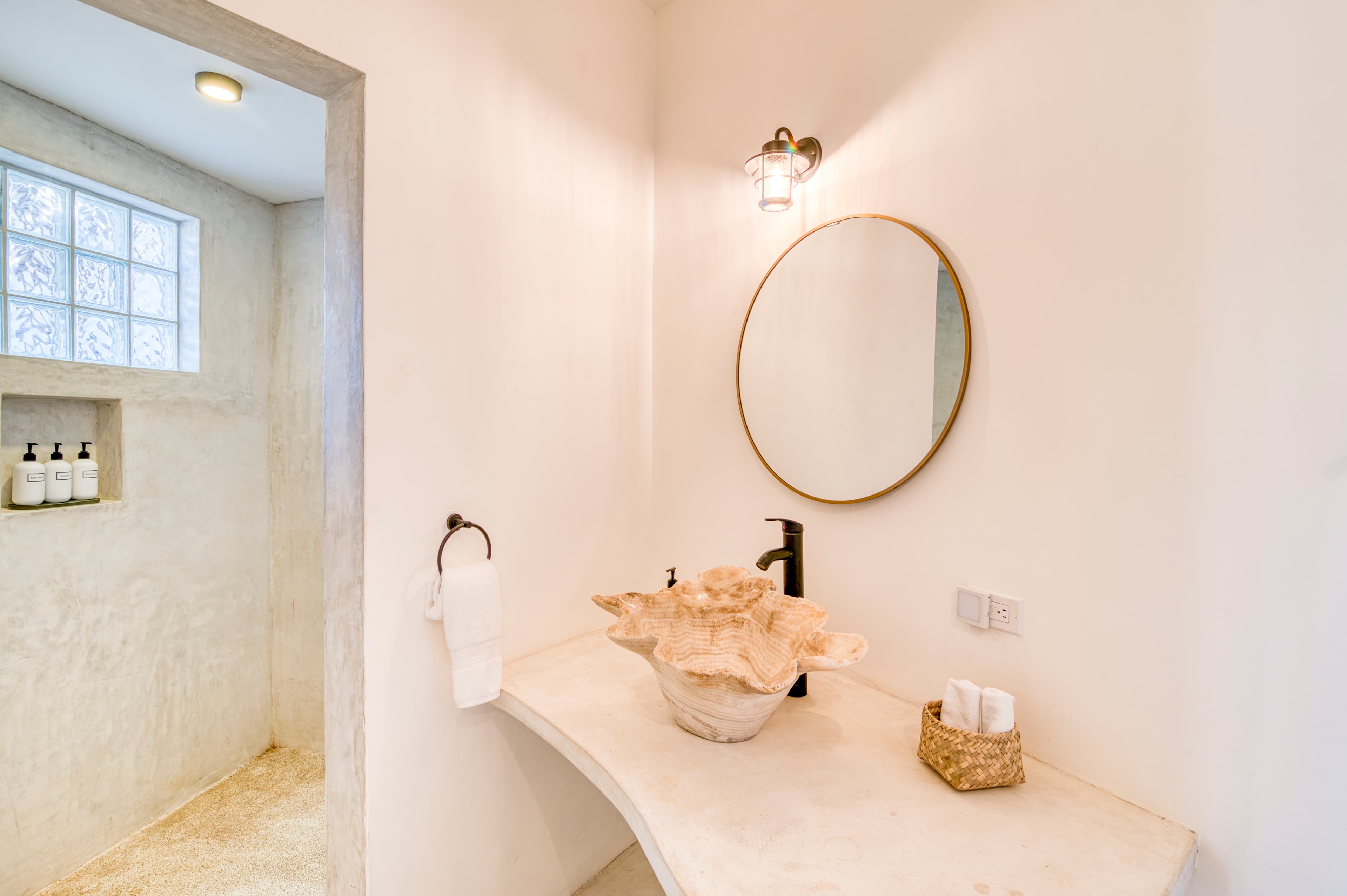 A minimalist bathroom features a curved stone sink, a round mirror, and a glass block window.