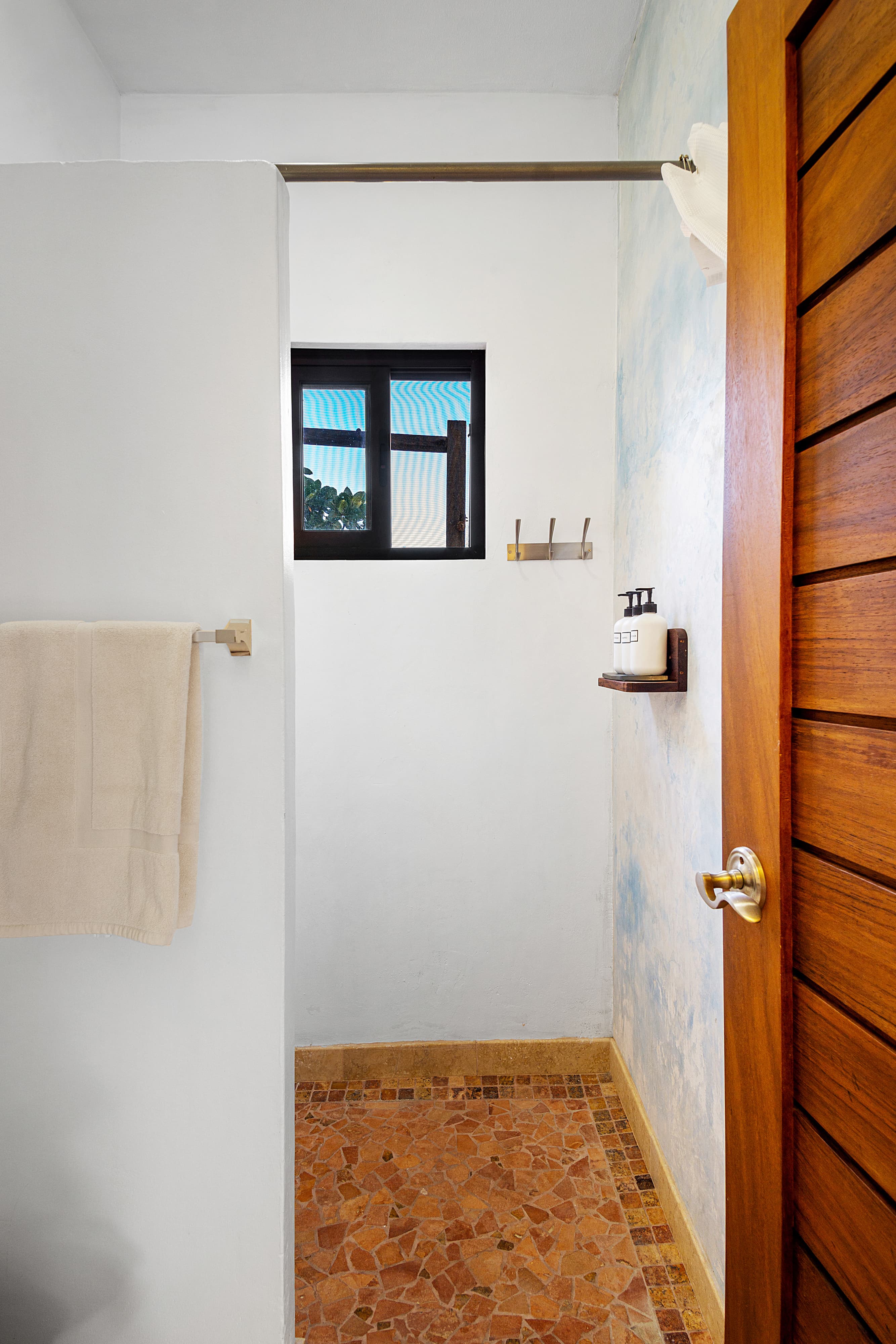 A bright, minimalist bathroom featuring a towel, a window, and a small shelf with toiletries.