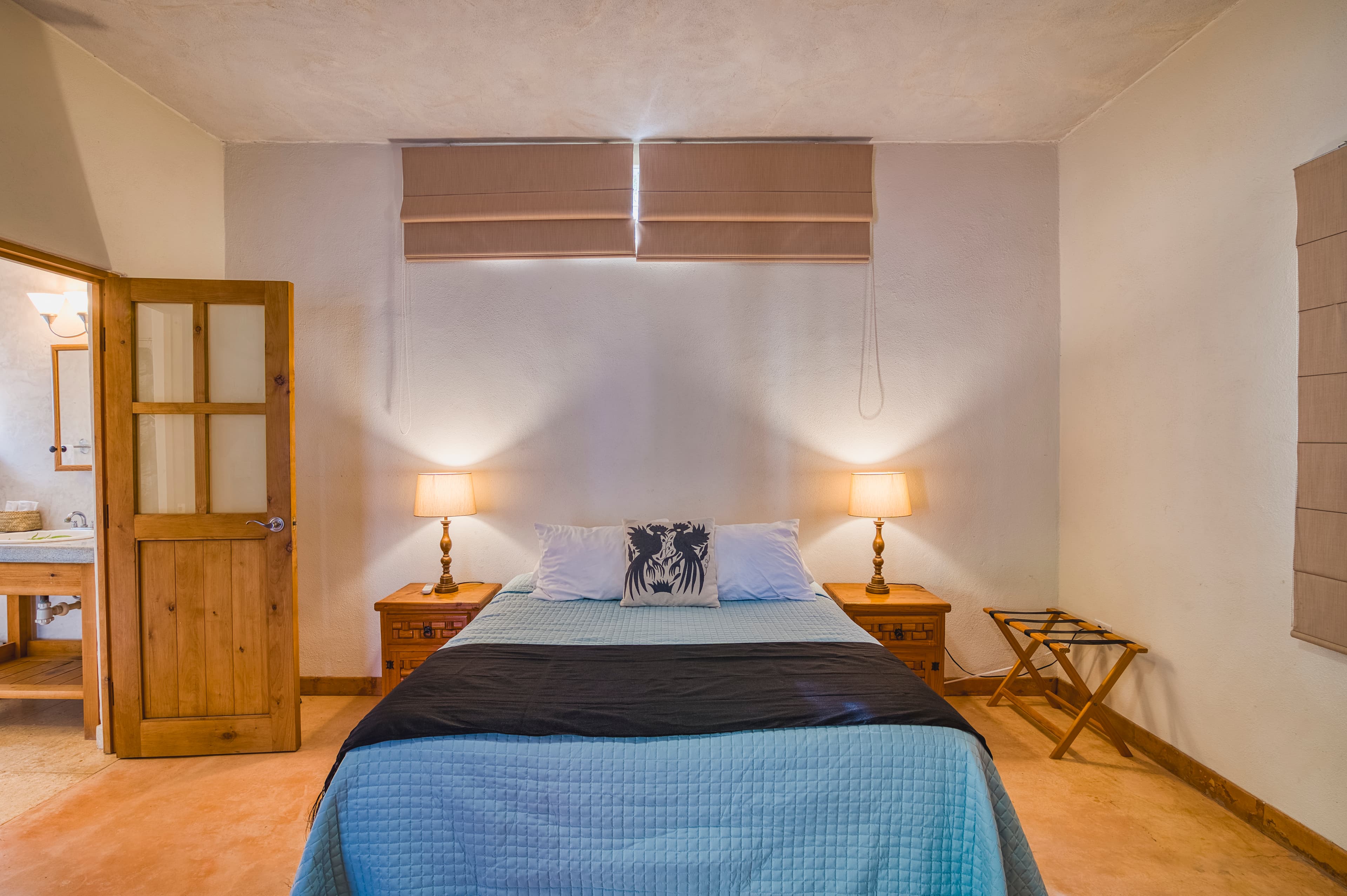 A cozy bedroom featuring a bed with a blue quilt, bedside lamps, and a wooden door leading to a bathroom.
