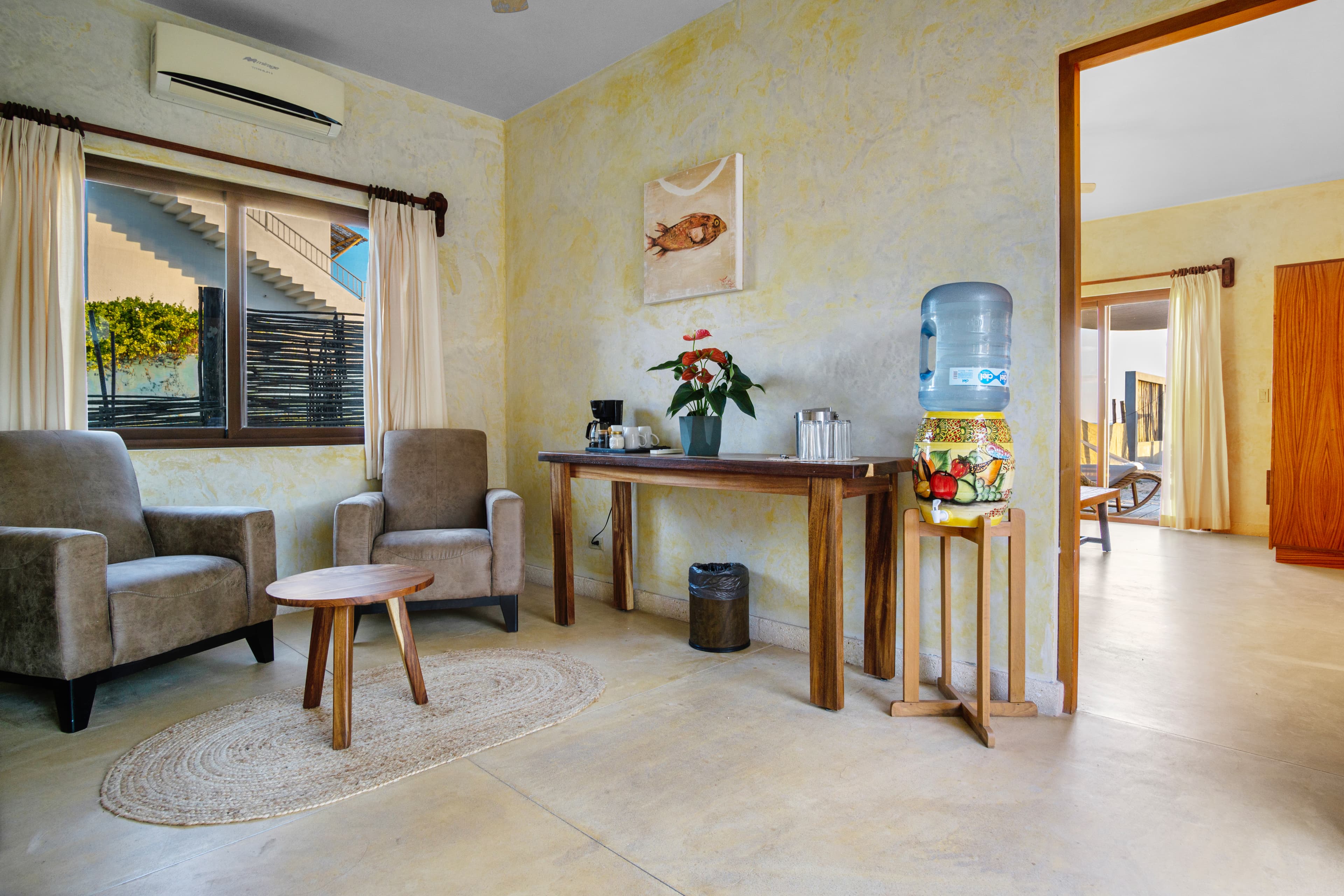 Cozy living area featuring two chairs, a wooden table, a water dispenser, and soft natural lighting.