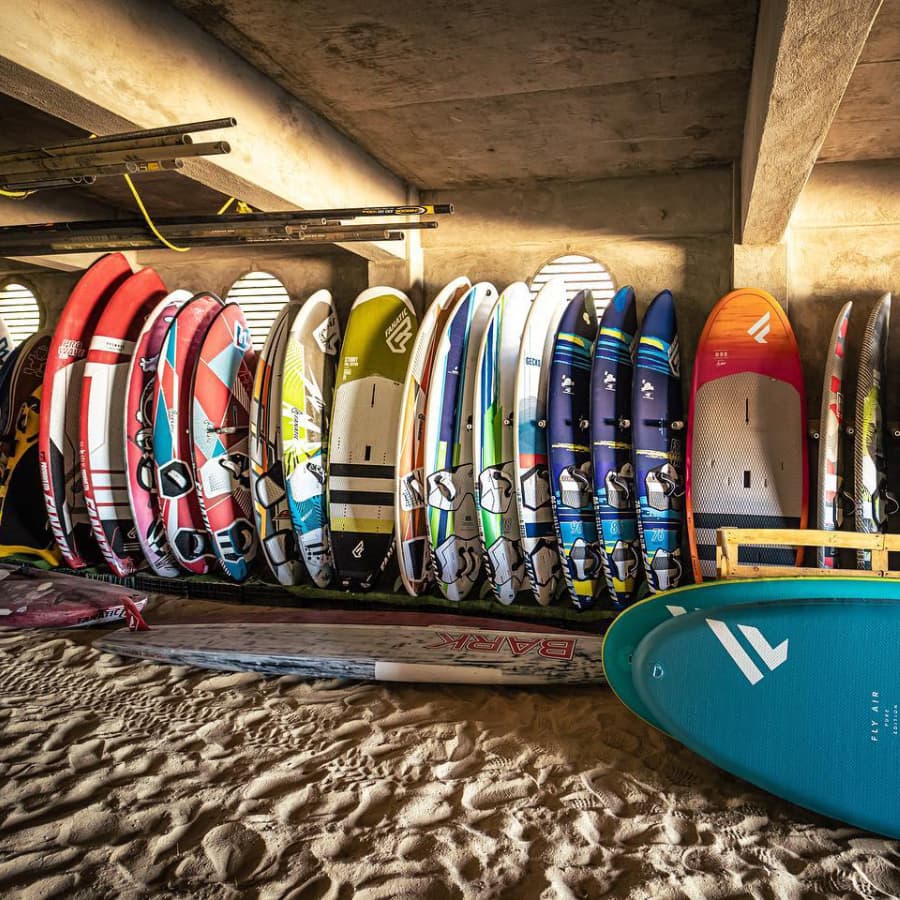A row of colorful surfboards neatly arranged on a sandy floor under a concrete structure.